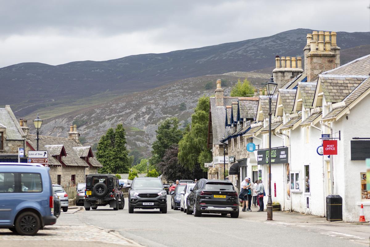 A streetscape with cars and shops and view to hills in the background.