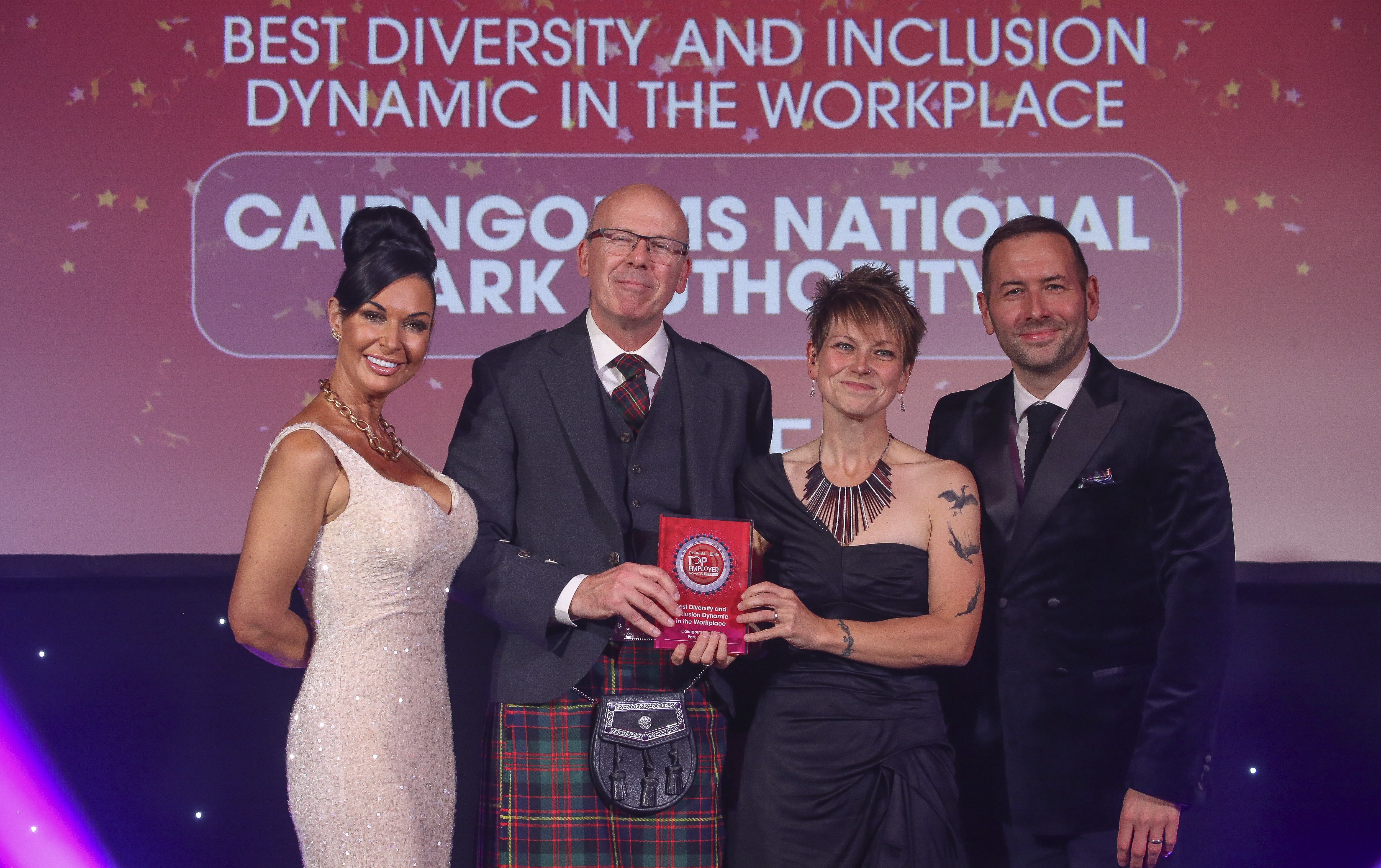 Four people standing on a stage, with two in the centre holding an award.