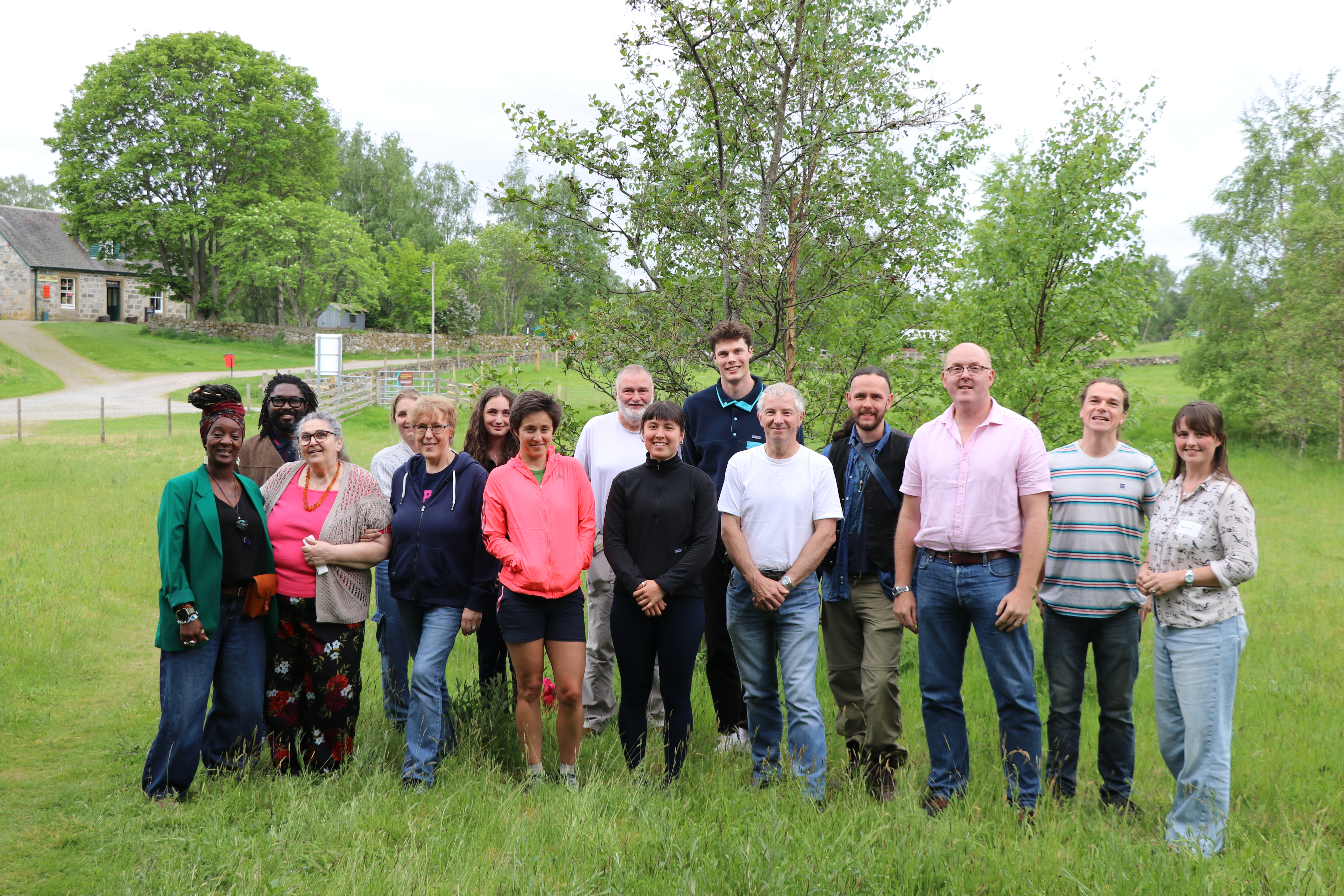 Group of people standing in grass smiling, with trees in background.