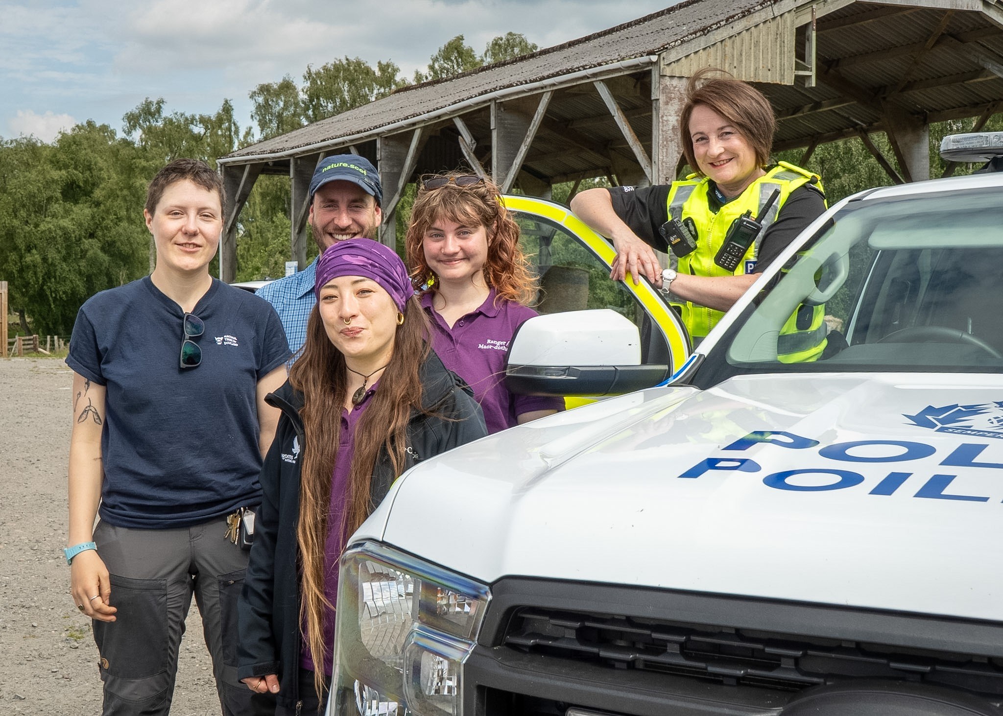 Five people (countryside rangers and a pollice officer) standing next to a police car with a shed in the background