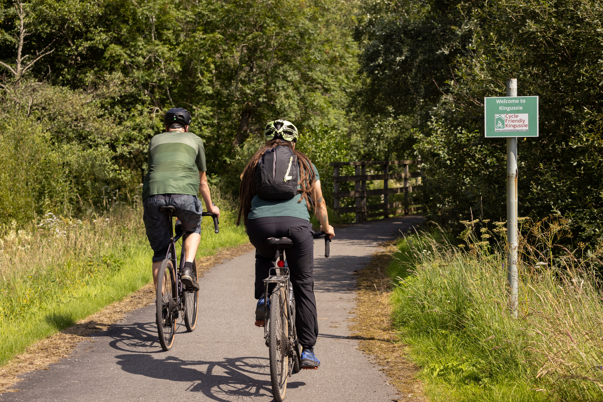 Two people cycling on a path past a 'Cycle Friendly Kingussie' sign