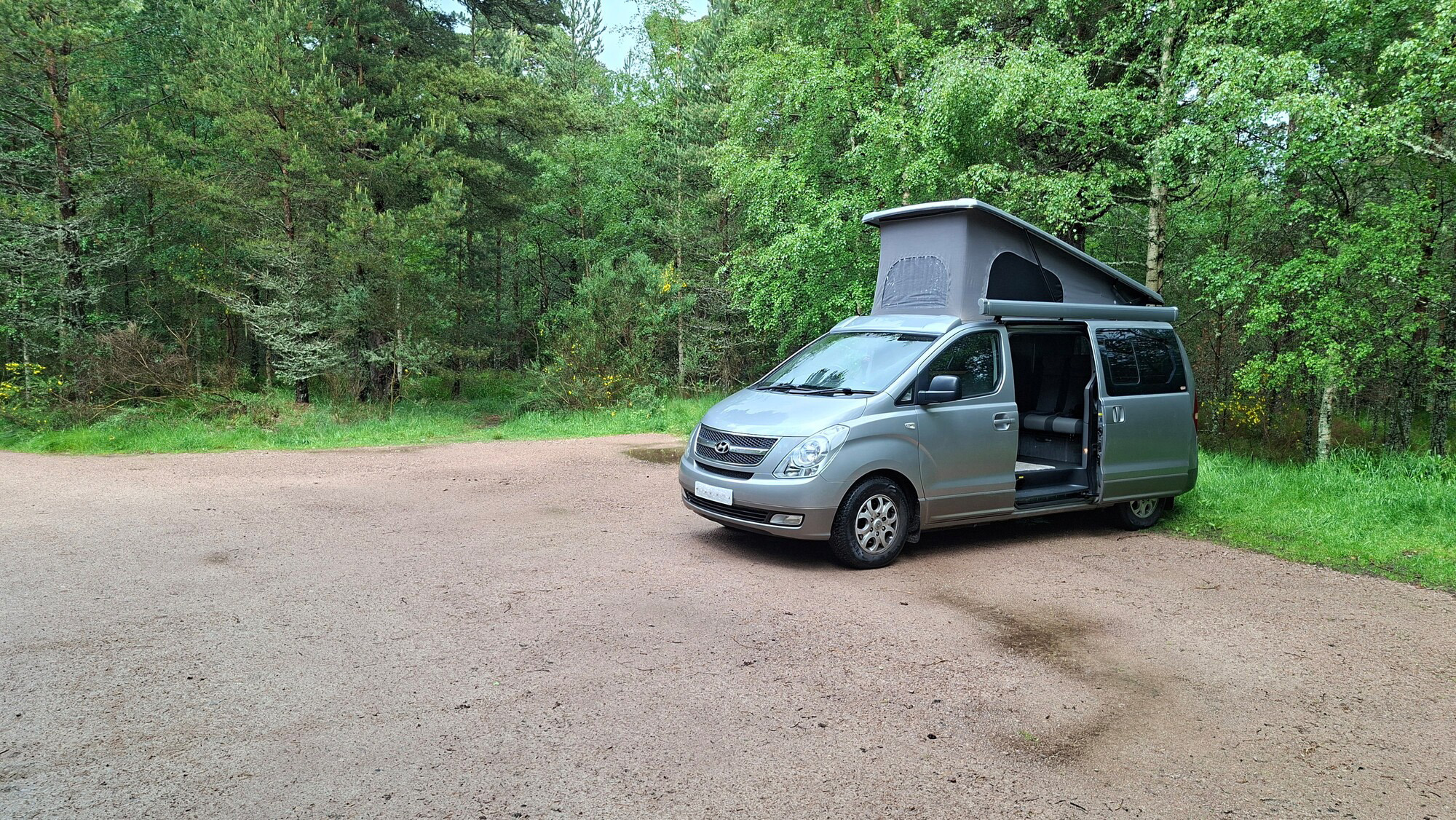 Campervan with roof up parked in woodland car park.