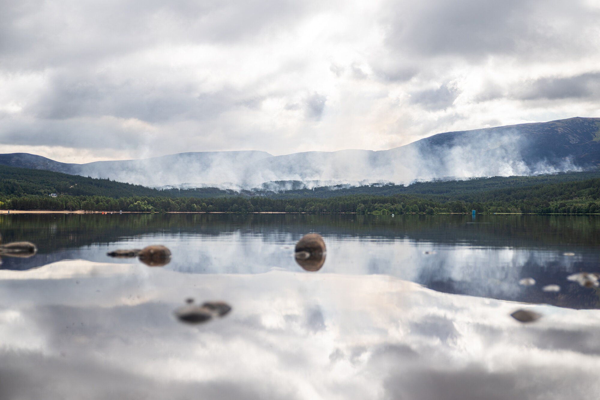 Smoke coming from the woods behind a calm Loch Morlich.