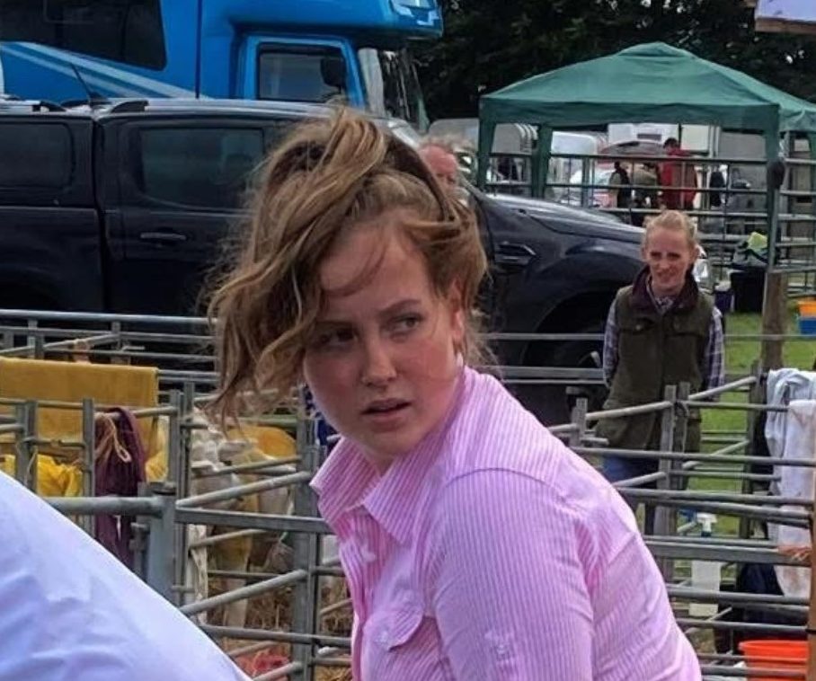 Head and shoulders of person in pink shirt standing in in front of cattle cages