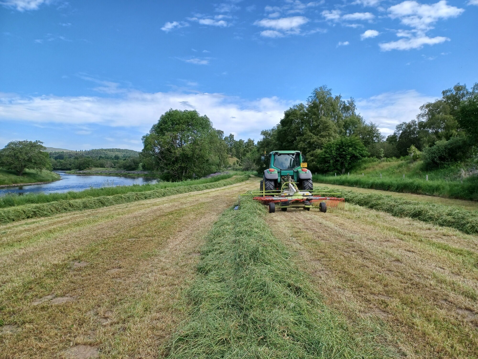 A tractor cutting grass in a field next to the river Spey.