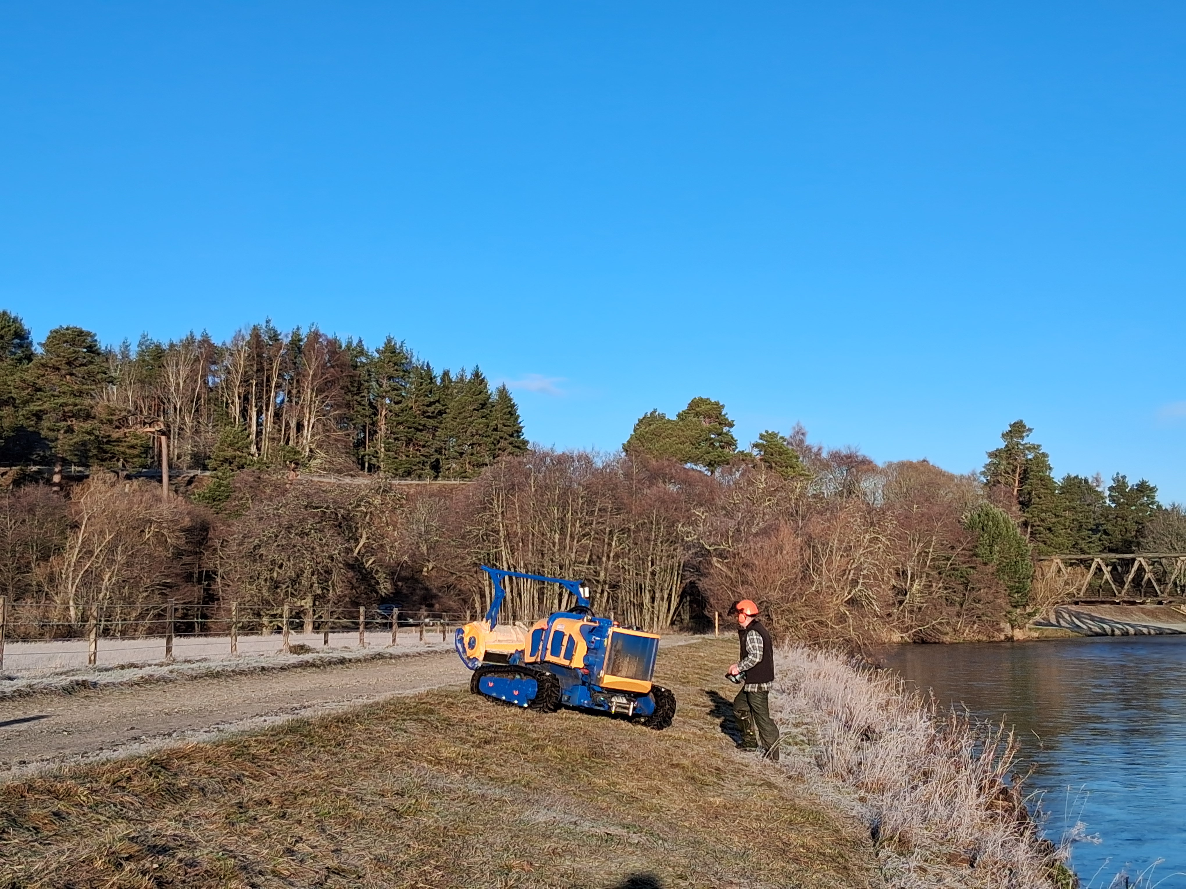 Local contractor using a yellow machine on a riverbank against a beautiful blue sky