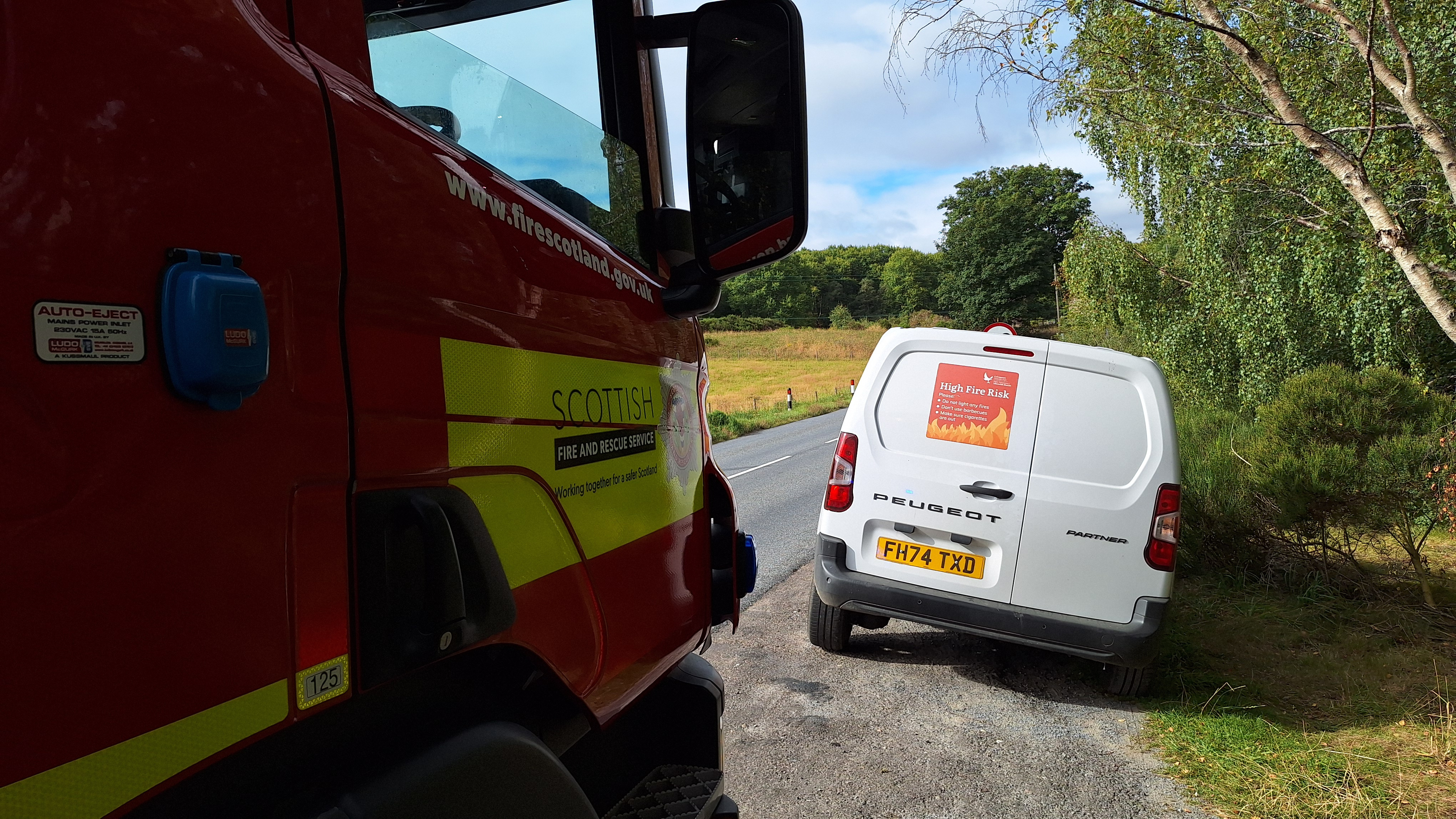 Part of a fire engine and the back of a white van with "high fire risk" signage on display.