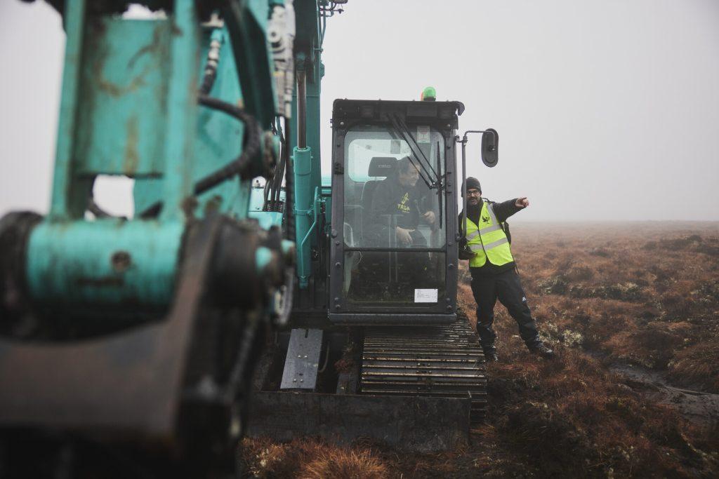 Image of Peatland ACTION Project Officer Ewan Campbell stood beside a digger with operator sitting in the cab on peatland restoration project.