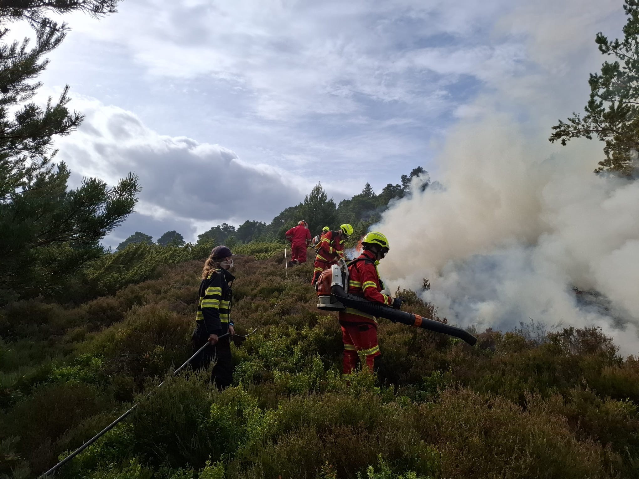 Four firefighters and one volunteer dressed in protective equipment fight a wildfire in Abernethy