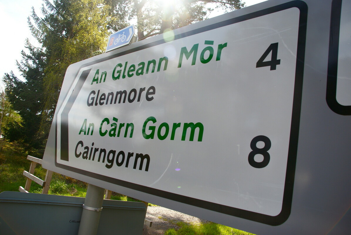 A road sign pointing to Glenmore (4 miles) and Cairngorm (8 miles), including Gaelic translations (An Gleann Mòr and An Càrn Gorm).