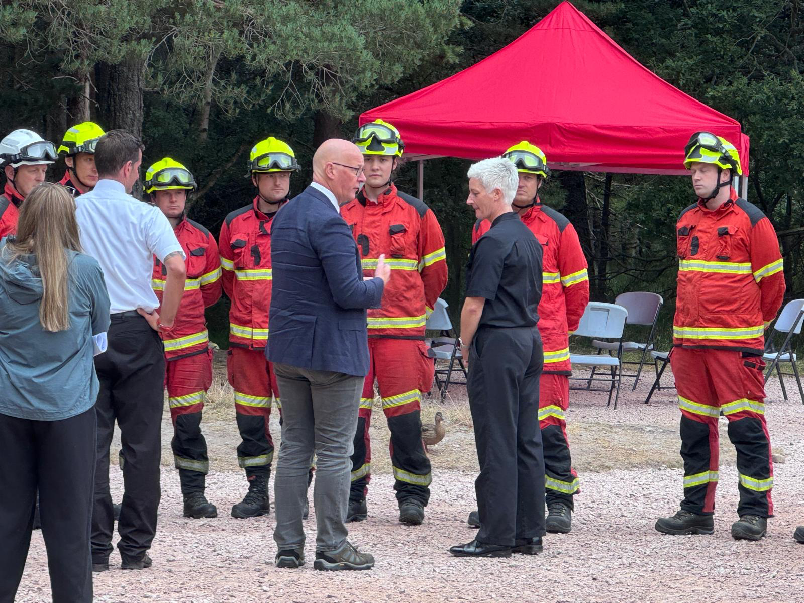 John Swinney talks to Area Commander Lynne Gow of SFRS, in front of a team of uniformed firefighters at Loch Morlich