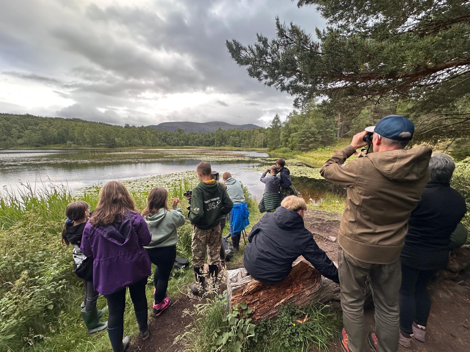 A group of people next to a loch looking for beavers