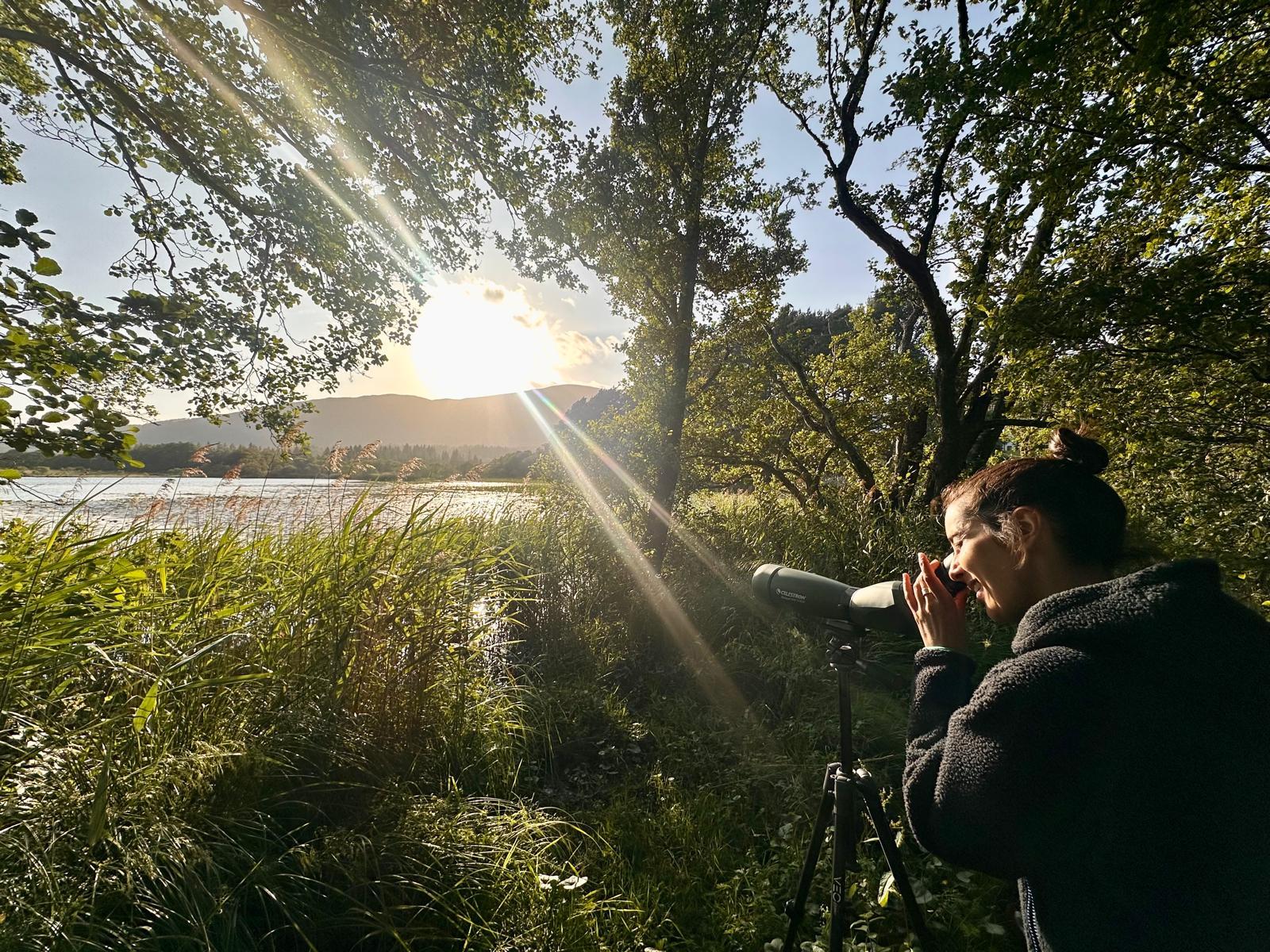 A person looking through a lense as the sun sets over a loch