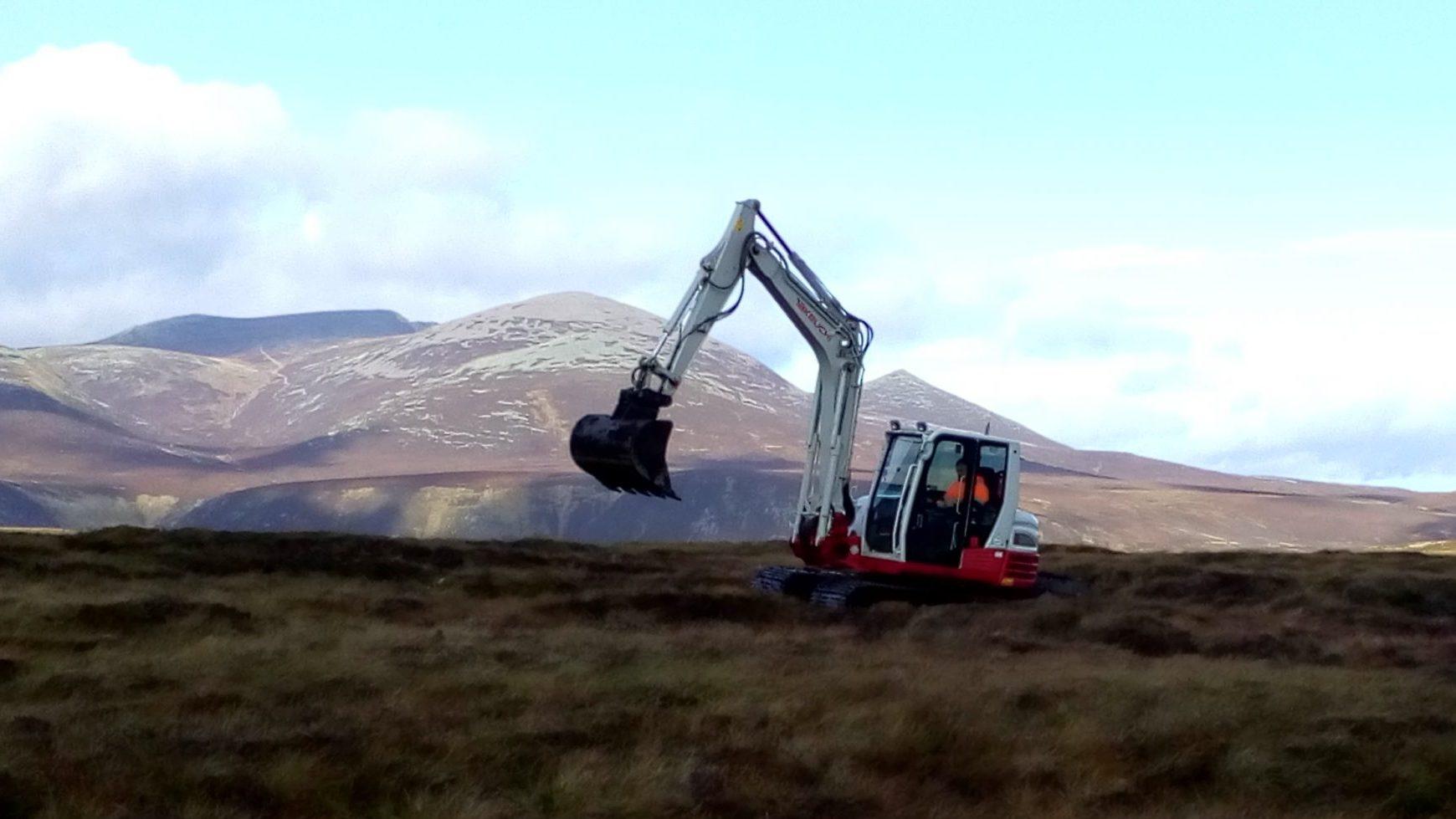 A digger working in remote location with mountains in background.