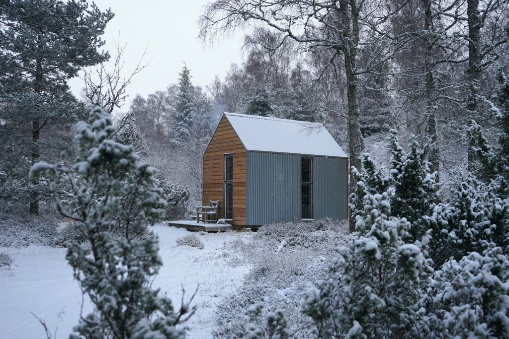 Image of Inshriach Bothy in snow covered woodland in the Cairngorms National Park.