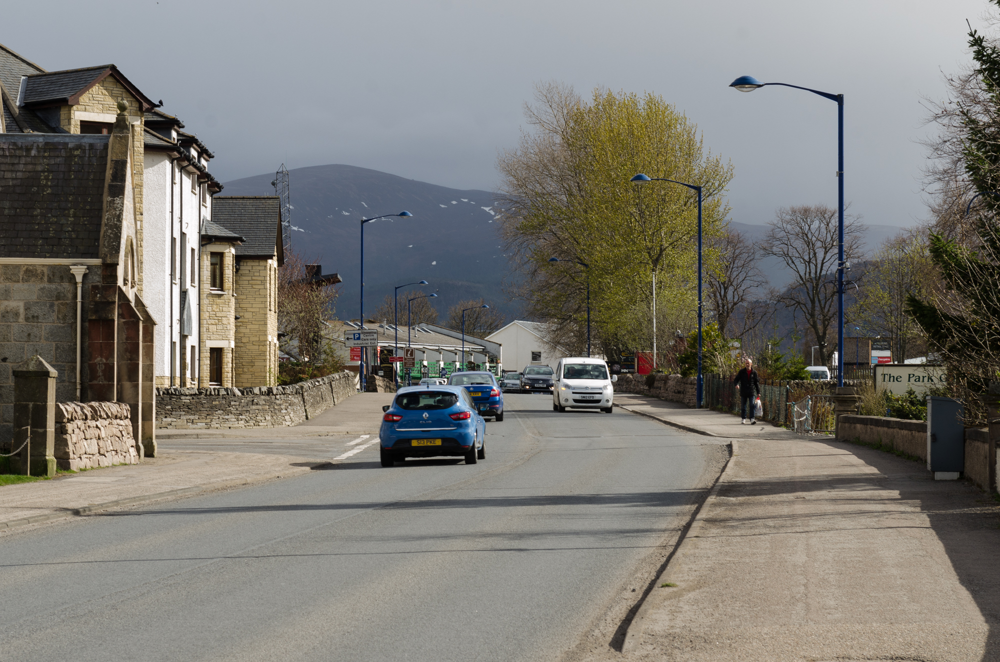 A street with a blue car and dark mountains in the background.
