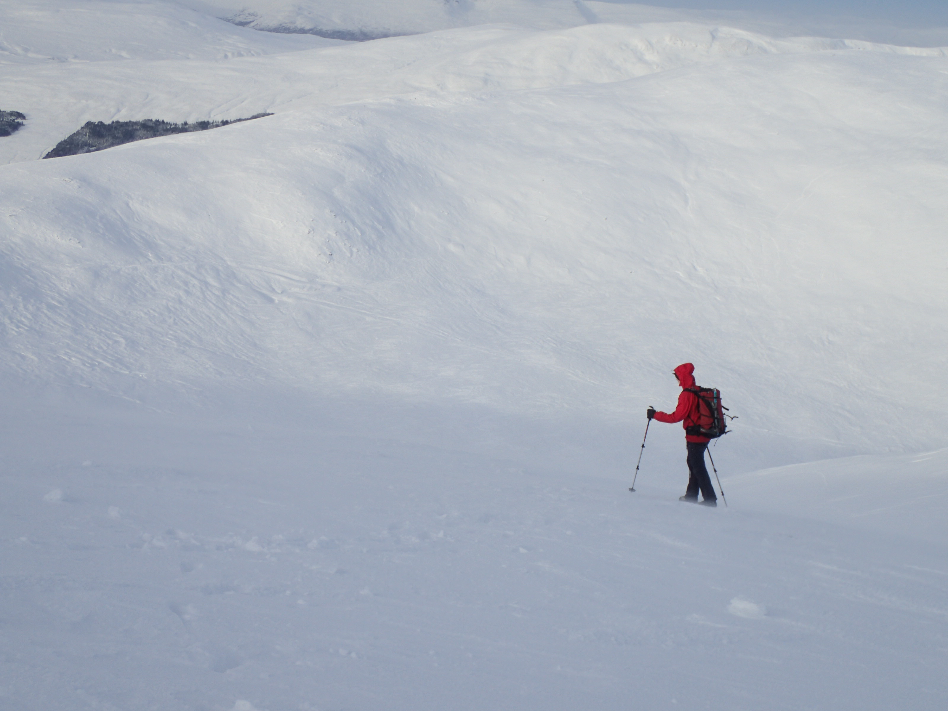 A person in a red waterproof and backpack treks through snow