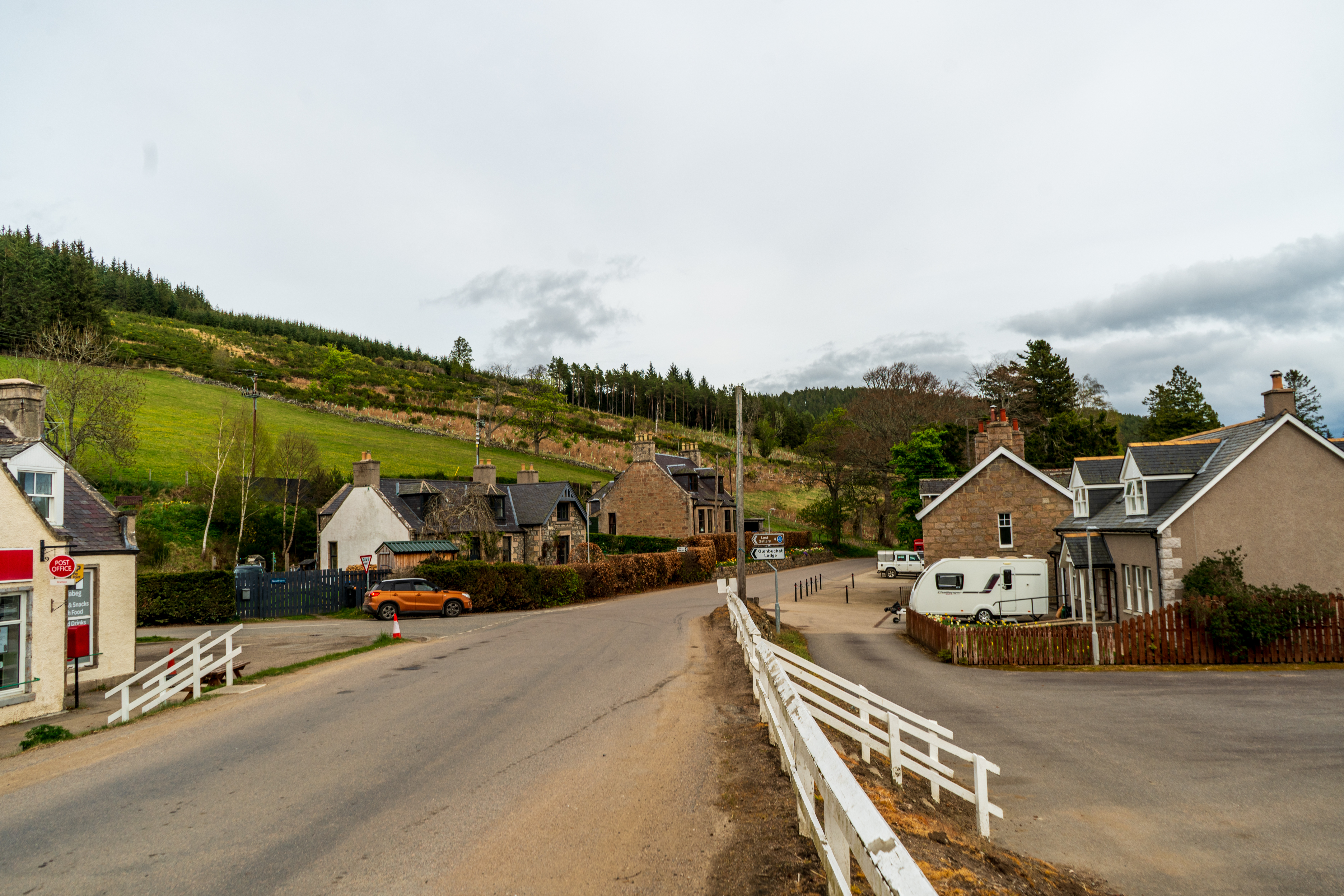 A street with houses and a green hill up to the left.
