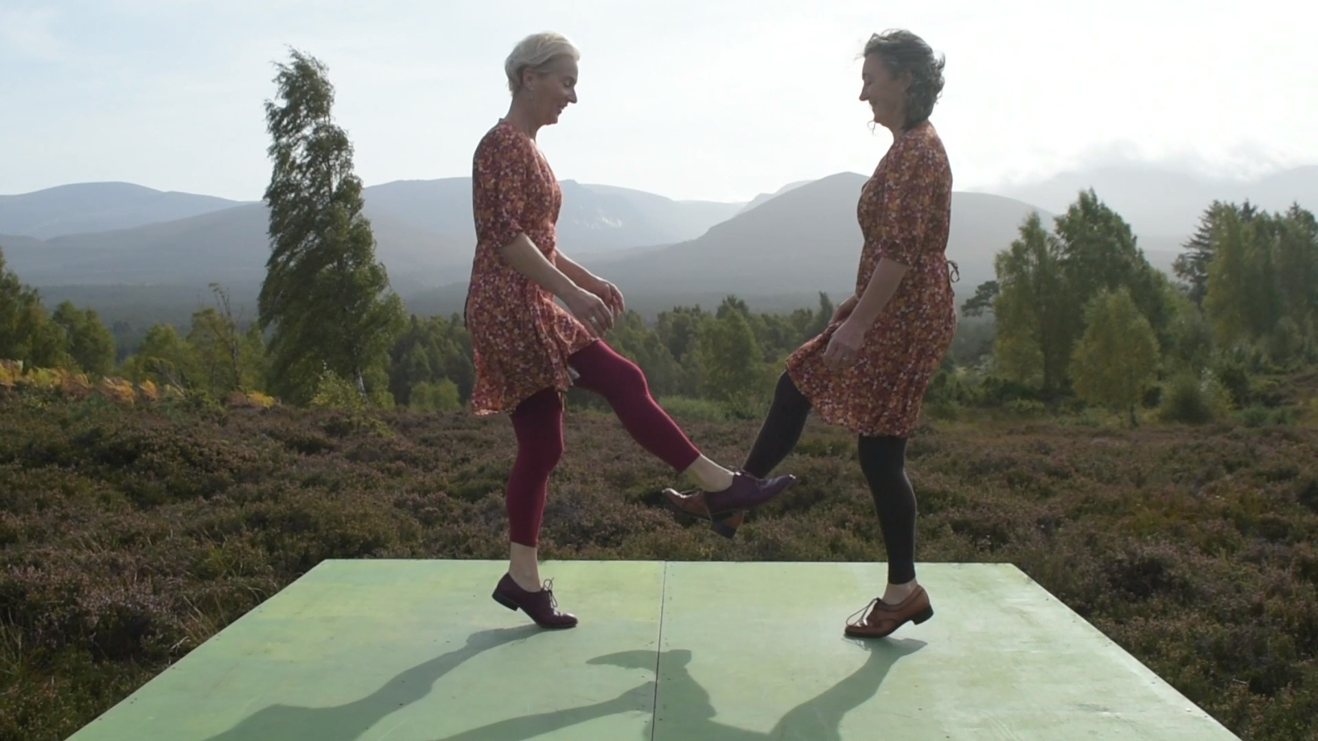 Two females doing a traditional dance with mountain landscape in background.