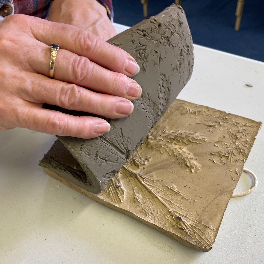 A hand pealing back a clay casting of foliage.