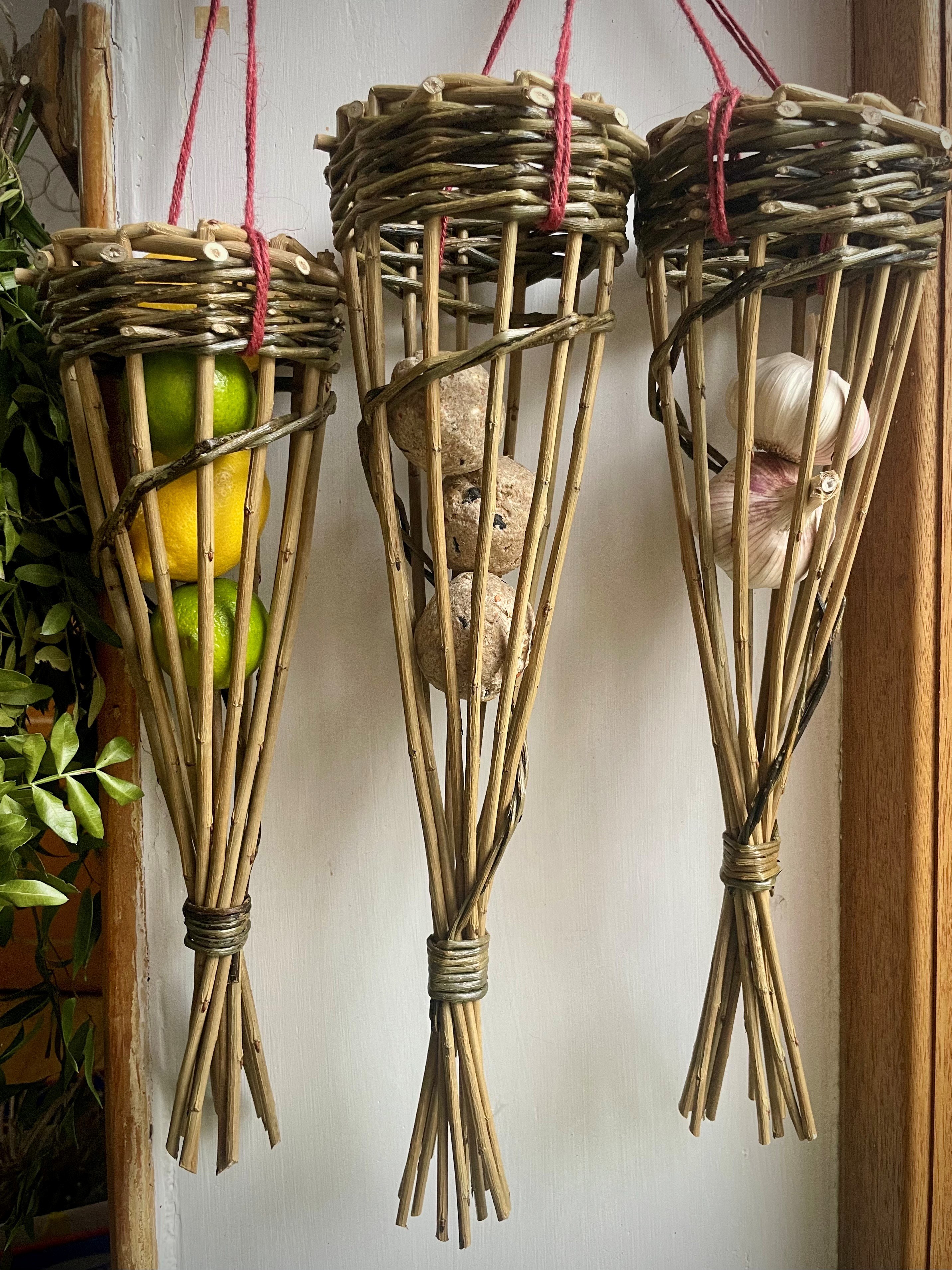 Three birdfeeders made from willow holding citrus fruit, fat balls and garlic.