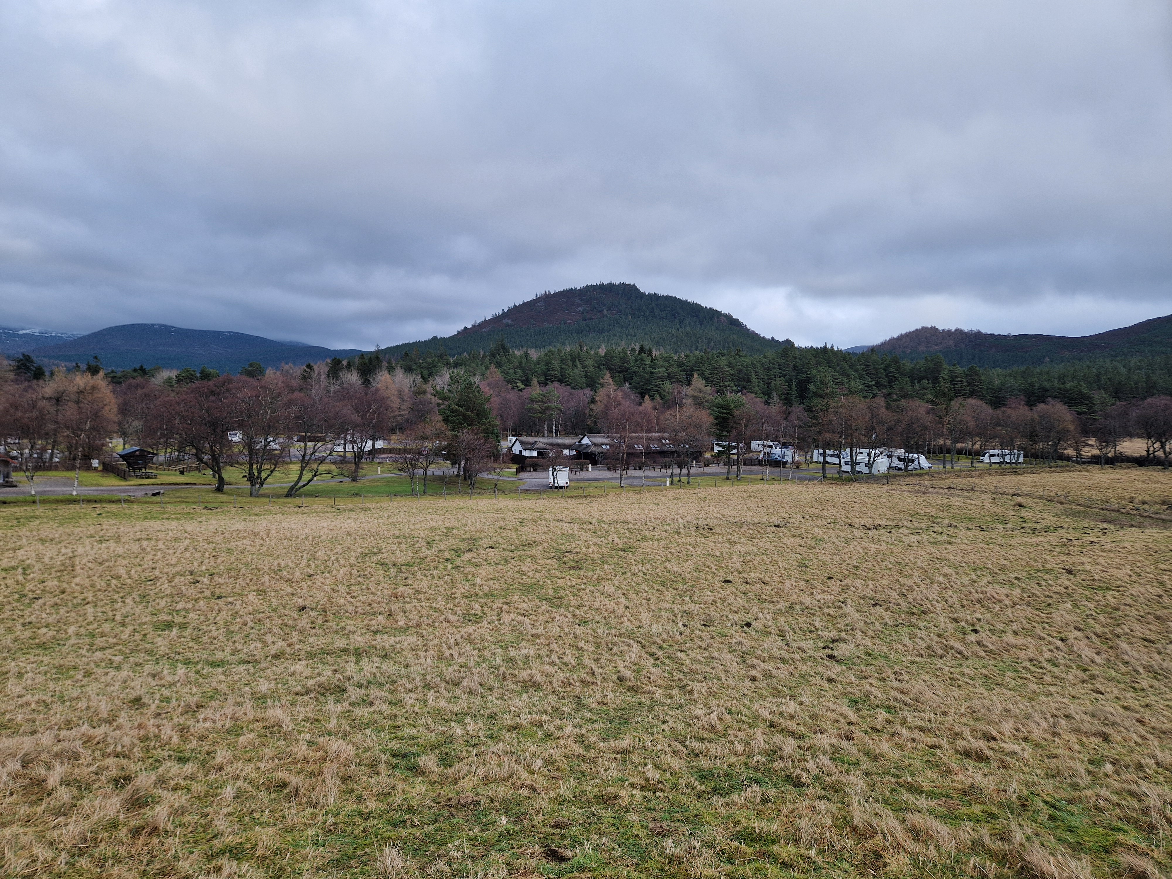 View of a field with trees, a caravan park and hills in the background.