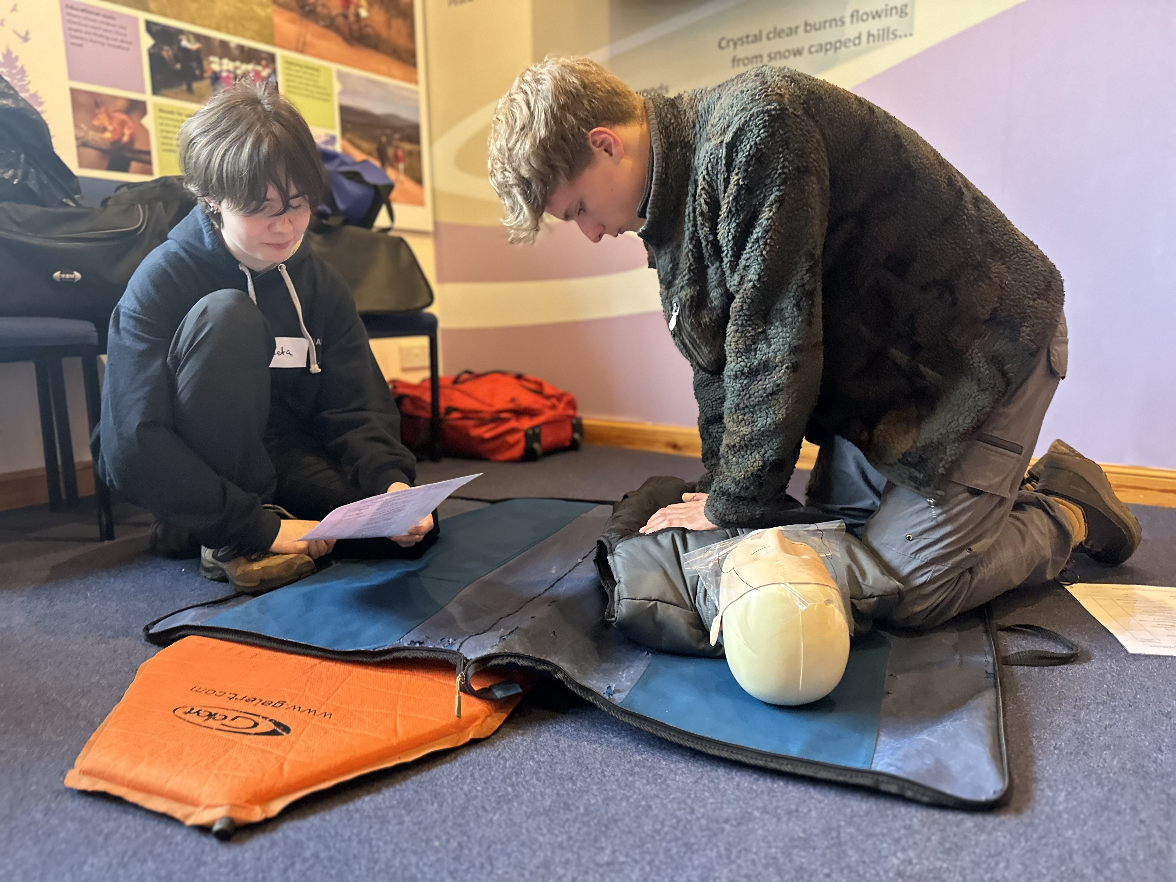 Two young people practising CPR on a first aid dummy