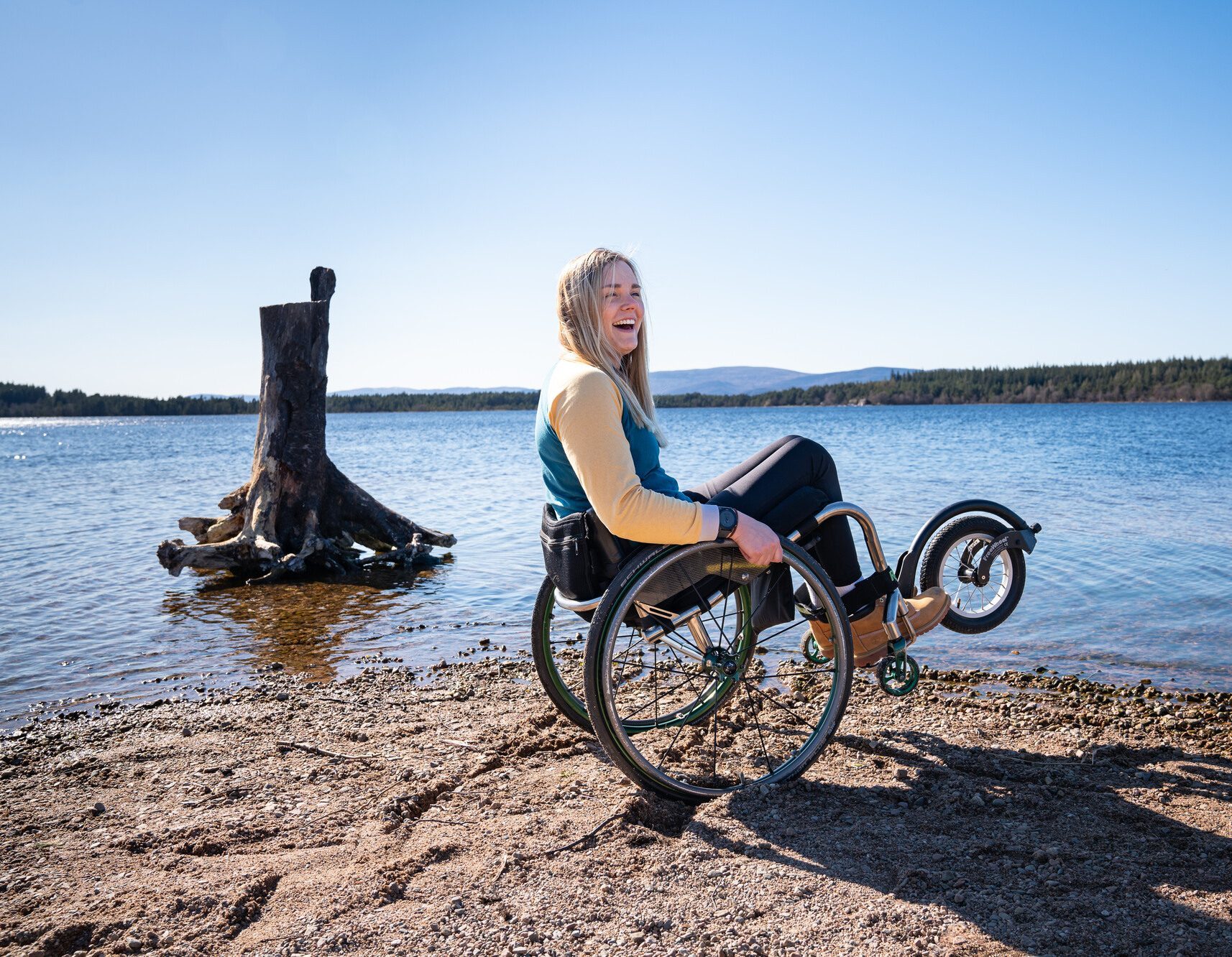 Person in an offroad wheelchair tilted onto two back wheels on the beach at Loch Morlich.