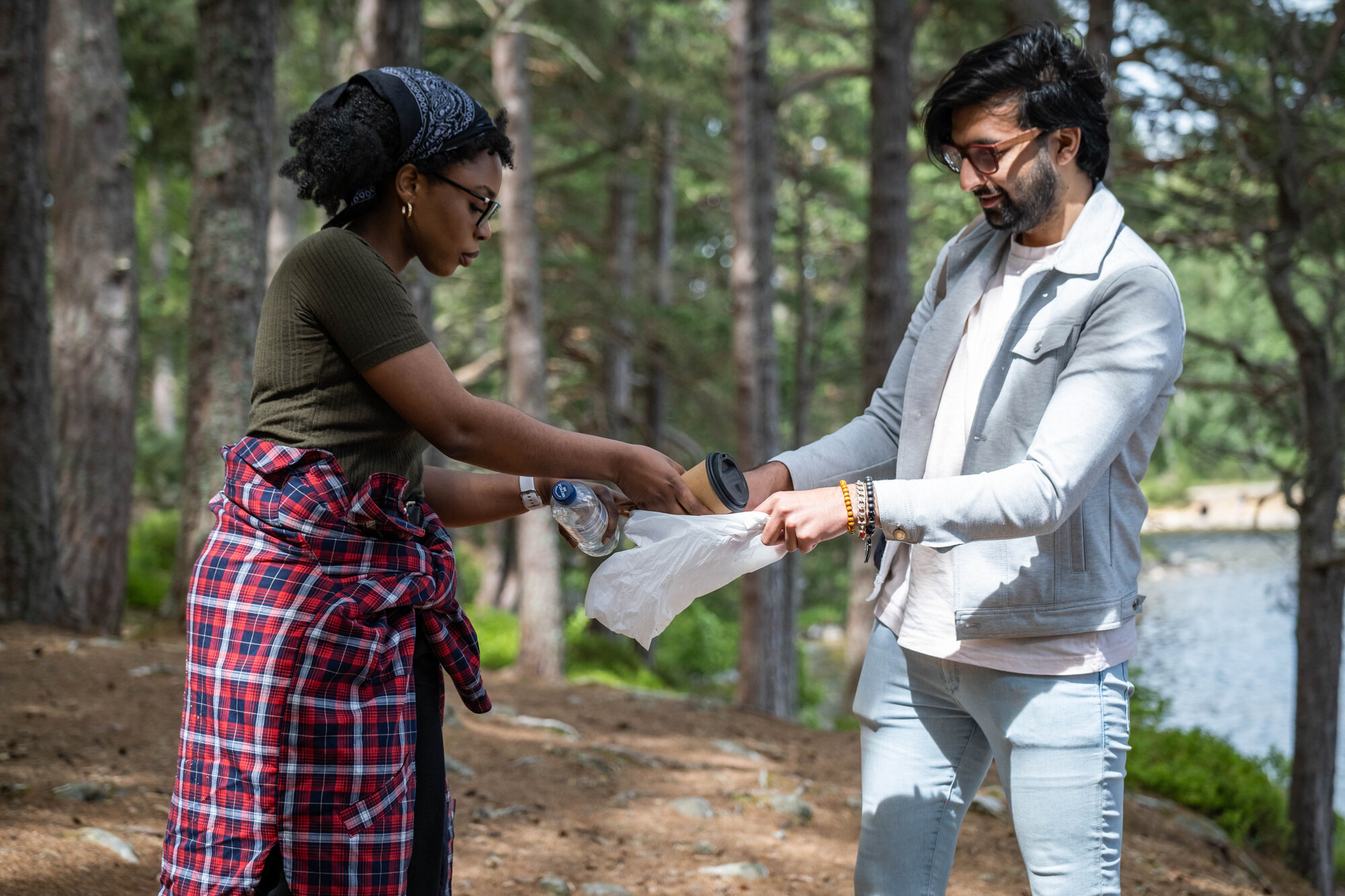Two people putting rubbish in a bag in the forest.