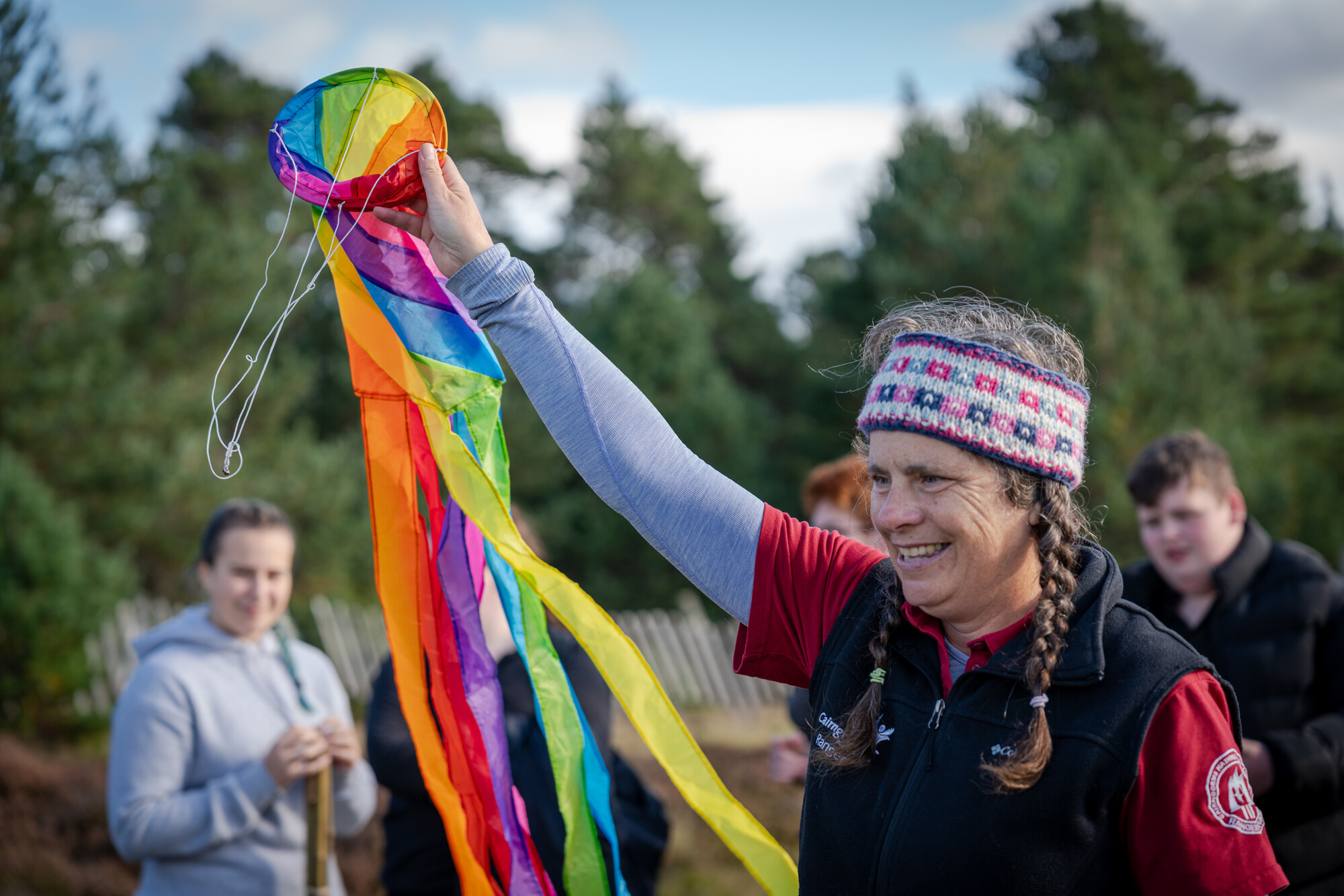 Ranger Polly holding a rainbow flag on a peatland monitoring site in the National Park with local school pupils in the background