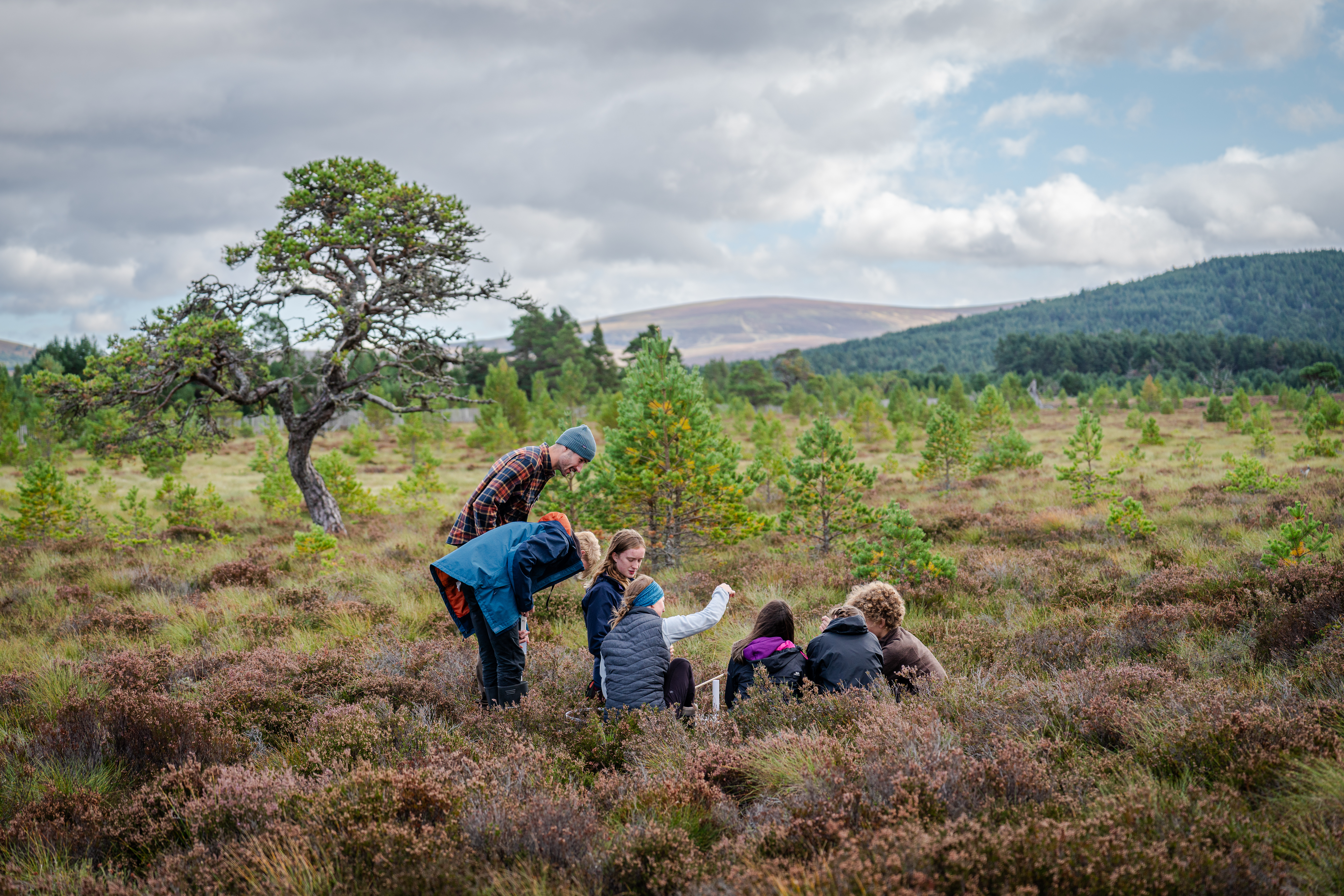 Young people gather round looking at the ground against a backdrop of mountains