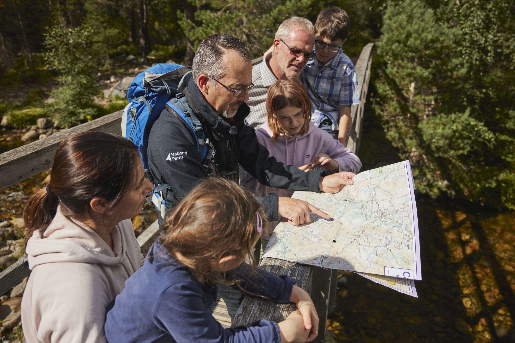 A ranger pointing at a map to show location to a family surrounding them.