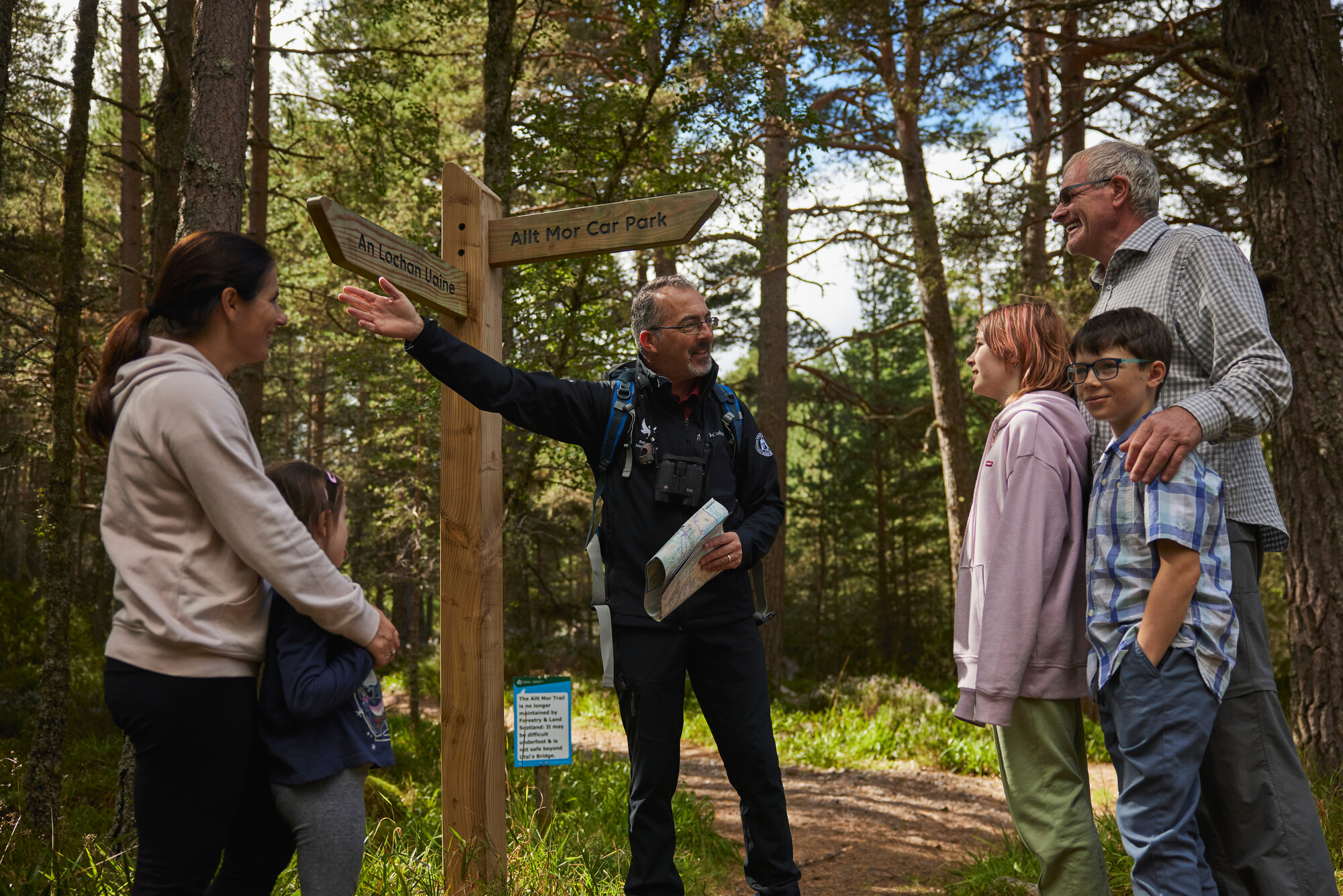 Forest scene with a countryside ranger in the centre of the picture pointing directions out for a family.