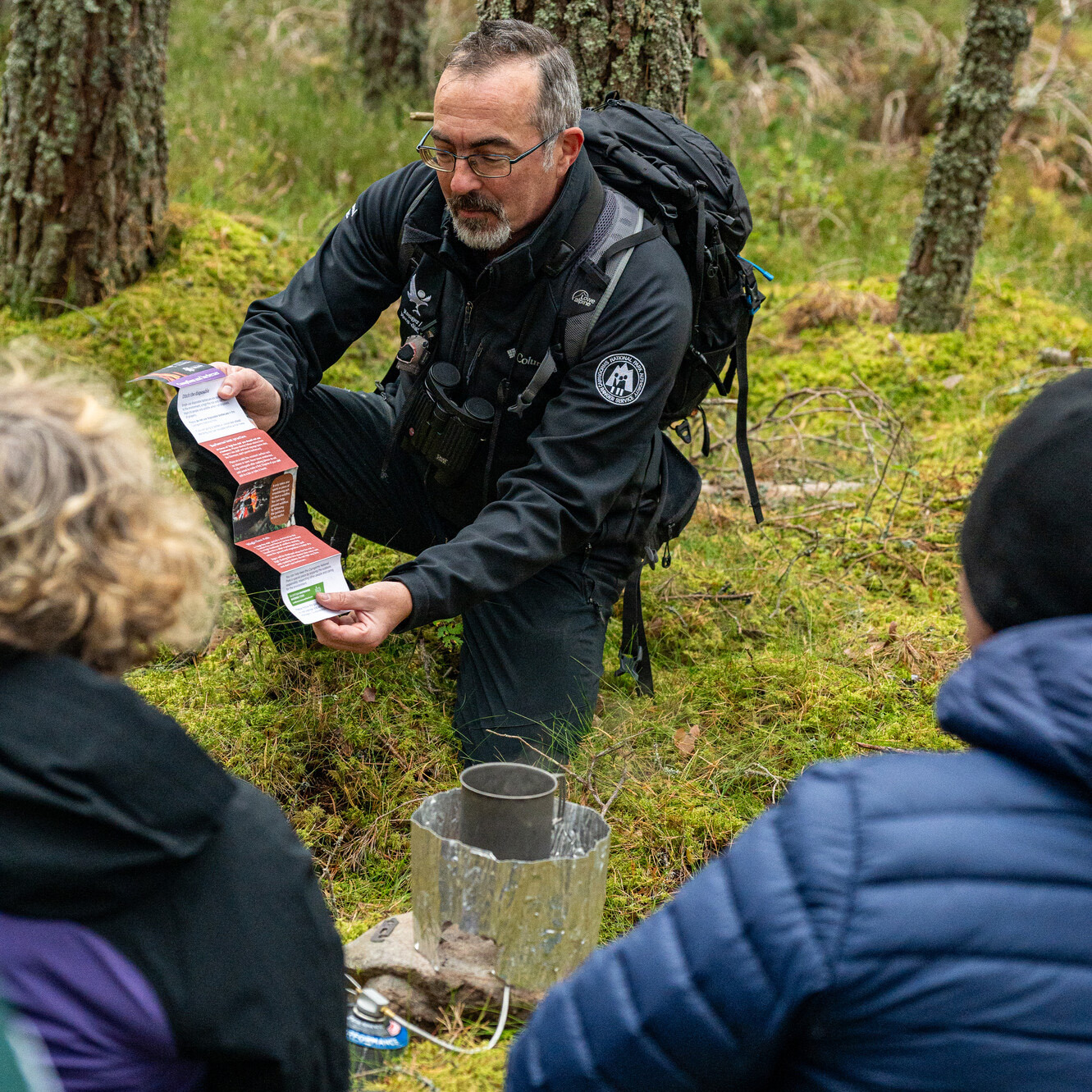 Countryside Ranger Duncan chats to 2 wild campers while out on patrol in a forest, offering advice, leaflets and appreciation for camping and cooking responsibly.