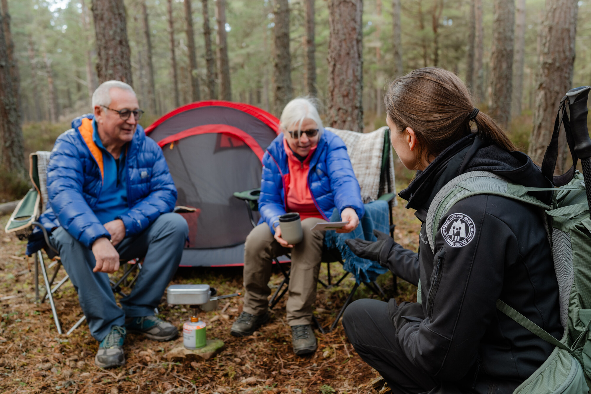Ranger engaging with campers with gas stove beside tent in woodland