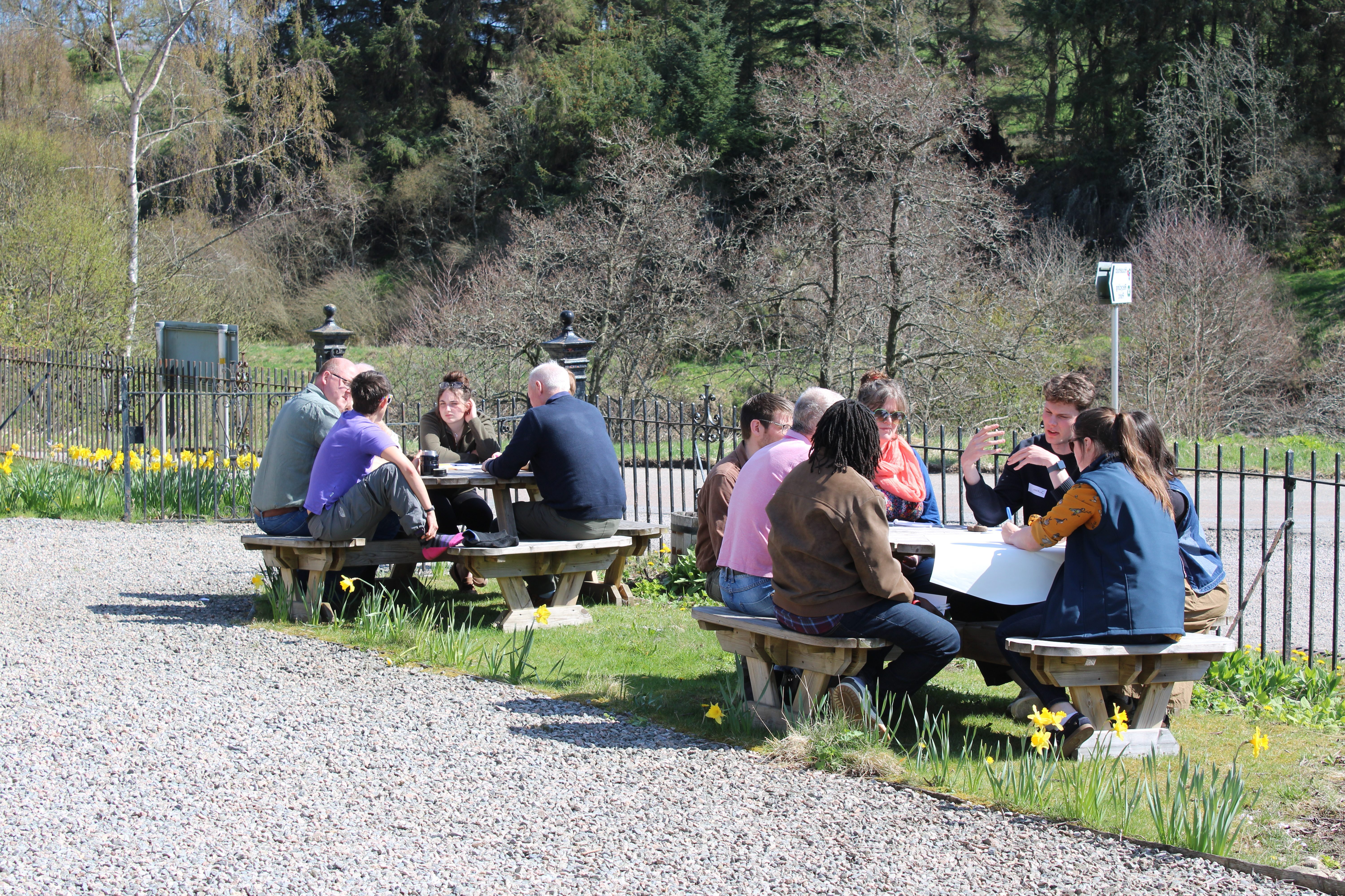 Two groups of people sit outside in the sun talking to one another