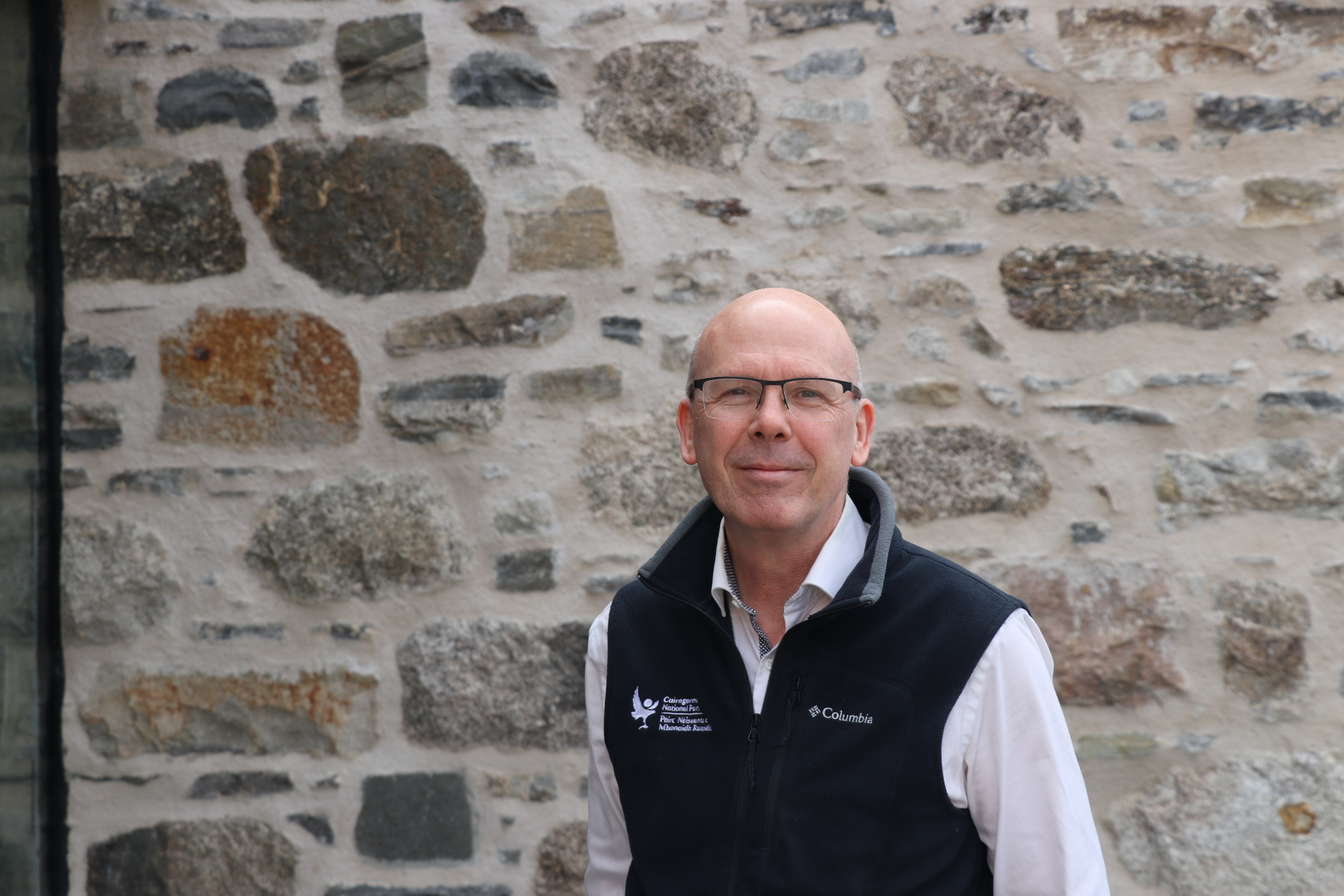 David smiles to camera against a stone wall