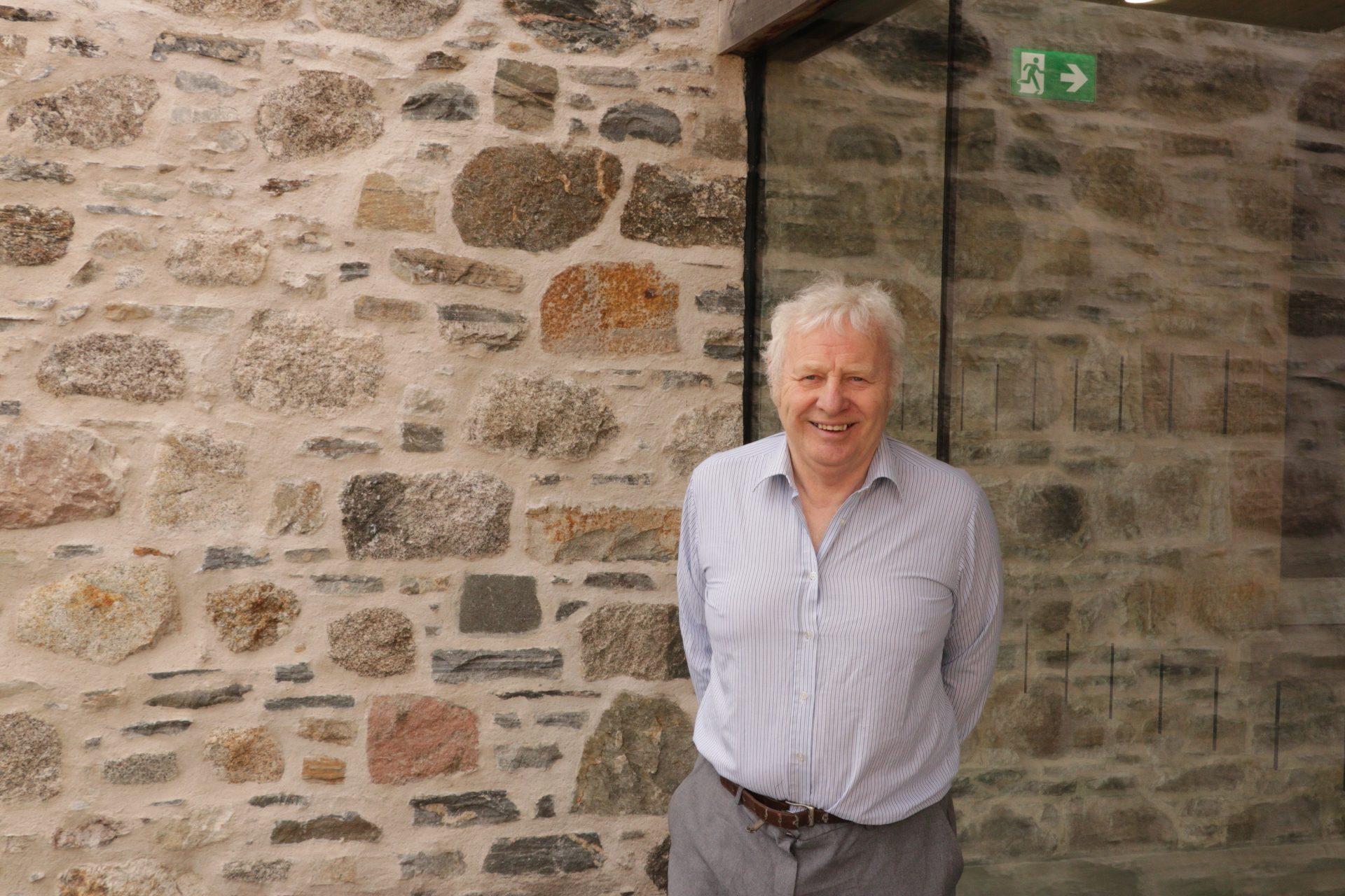 John Kirk smiles against a stone wall