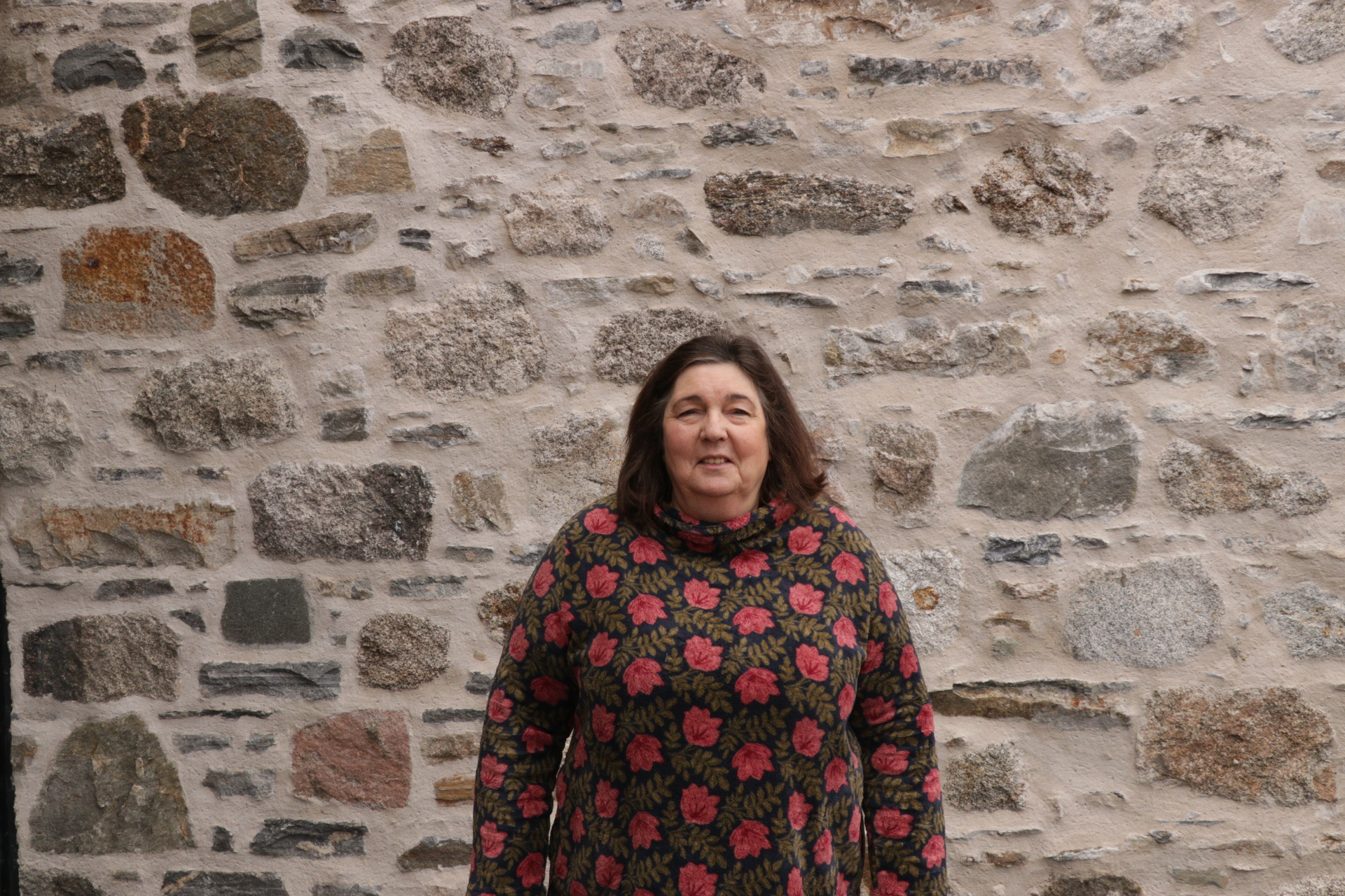 Geva smiles to camera against stone wall