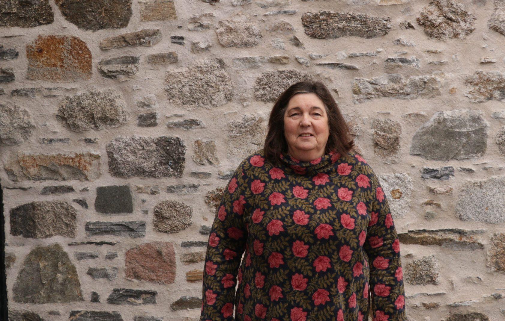 Geva smiles at camera with stone wall in background