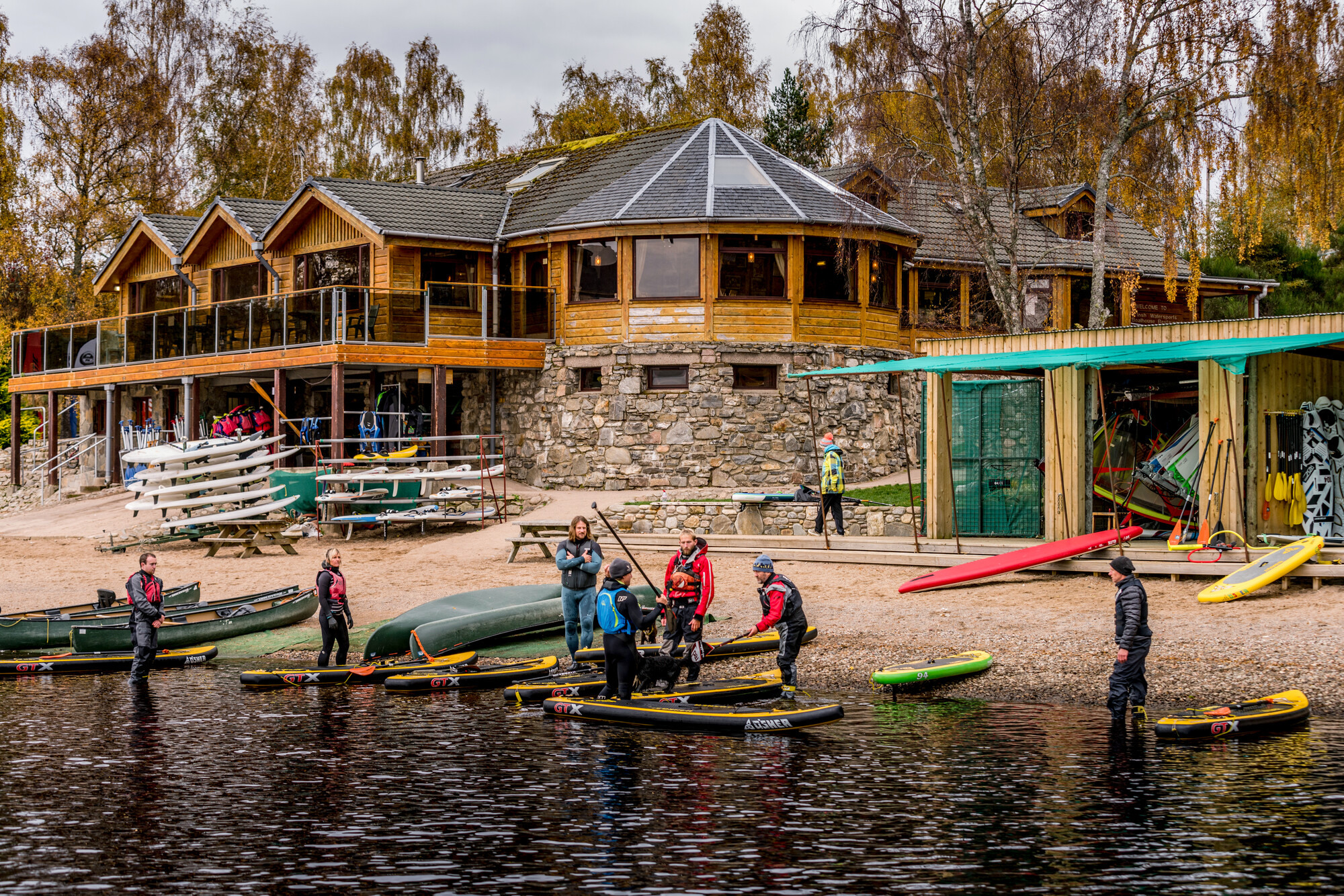 People preparing to go paddleboarding in front of Loch Insh water sports centre.