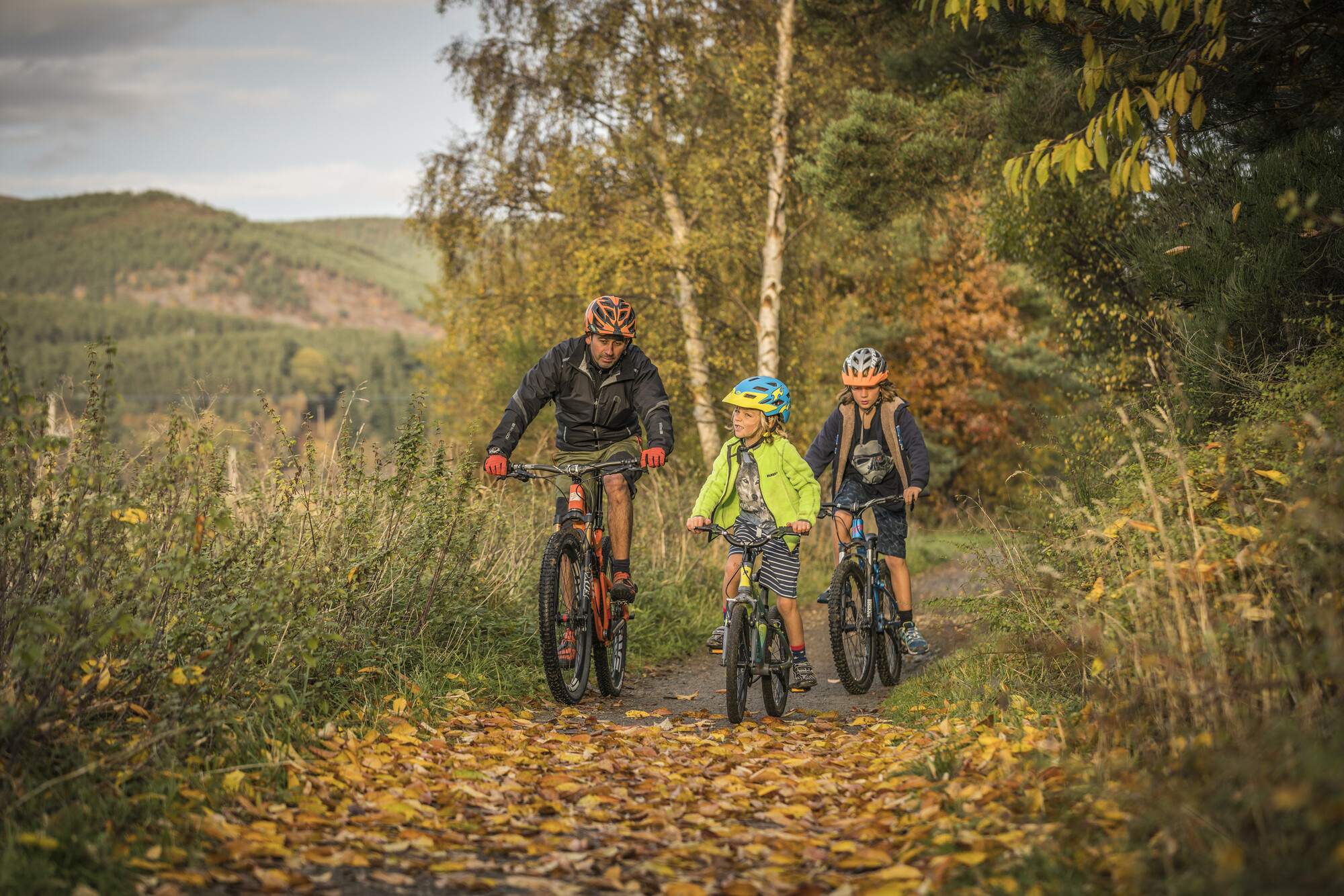 Three cyclists on a leaf covered woodland path