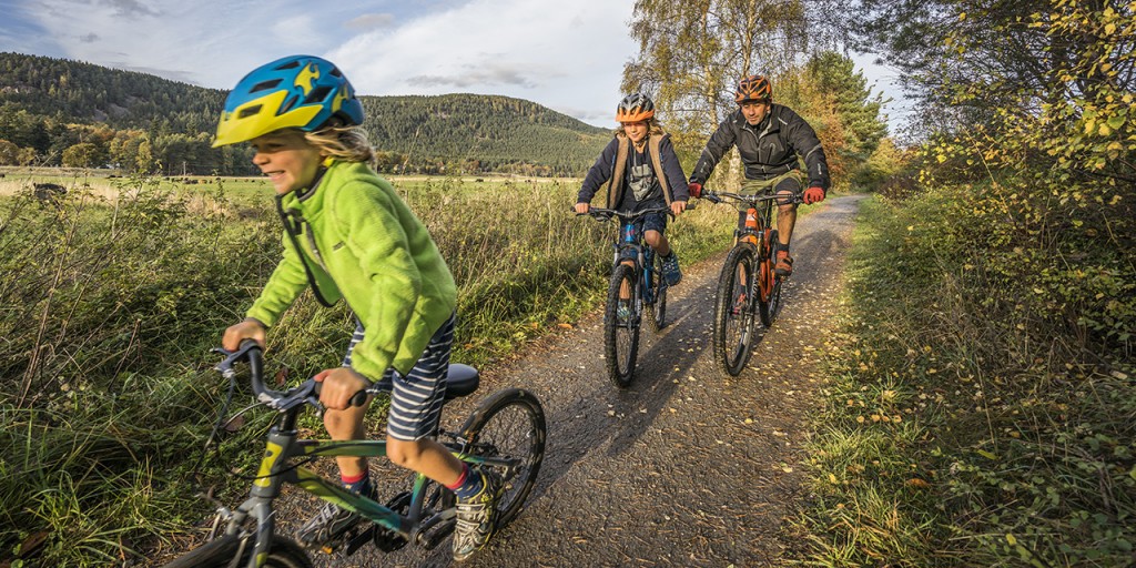 A family of cyclists follow the Deeside country paths during Autumn, the Cairngorms National Park.