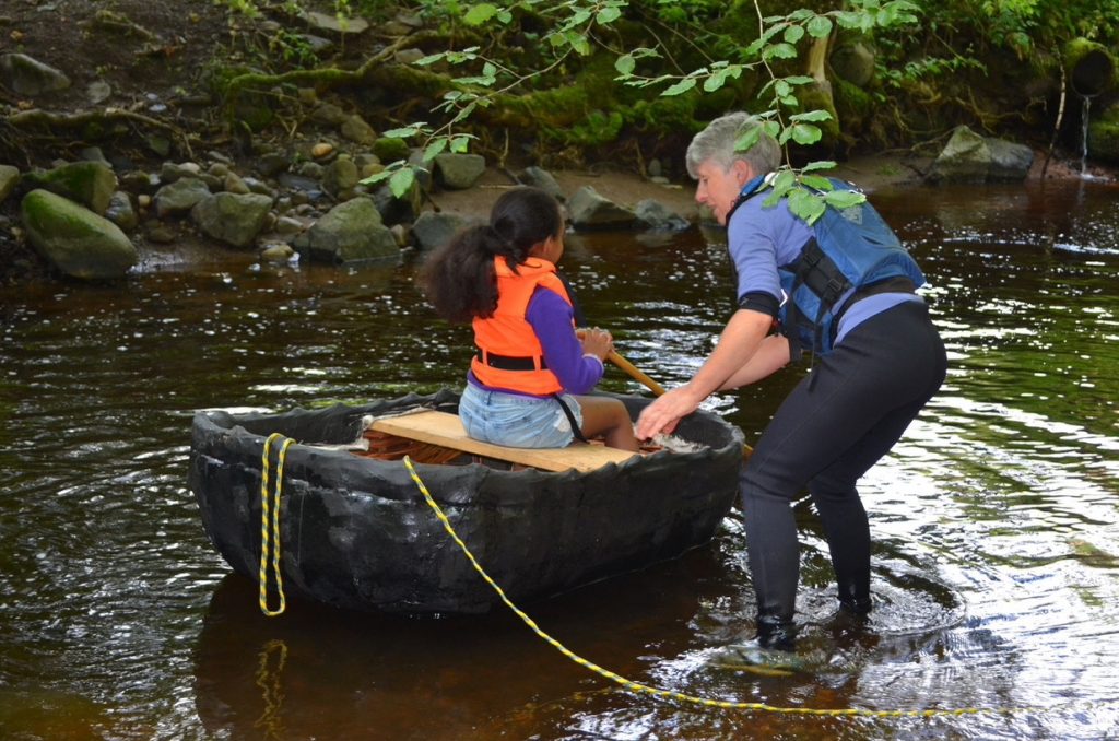 A girl in a traditional boat called a coracle being helped by a woman
