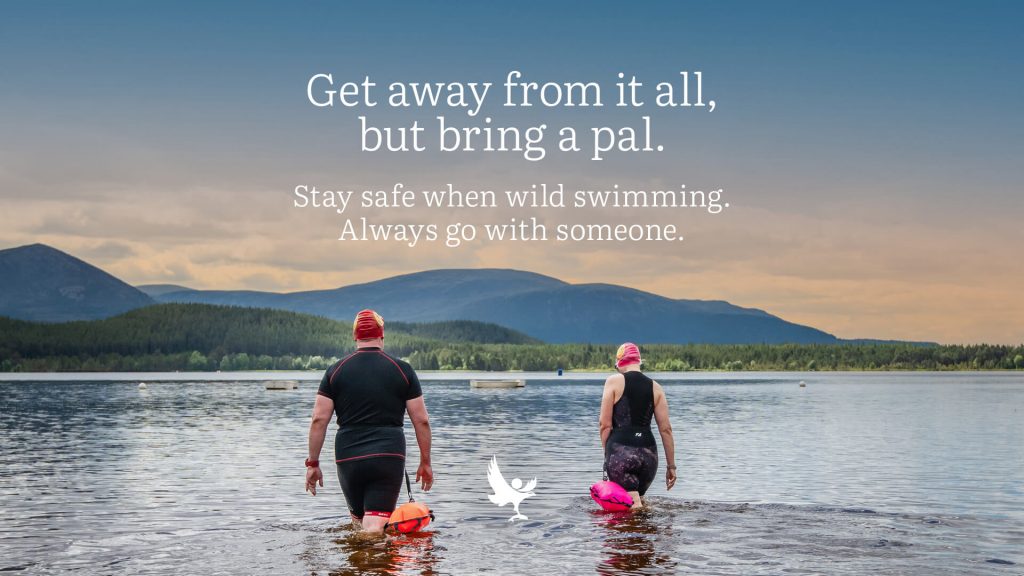 Two swimmers in a loch wearing safety floats and text message saying to stay safe and go with someone when wild swimming