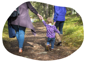 A young child holding a mother's hand walking on a scenic woodland path