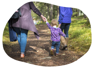 A young child holding a mother's hand walking on a scenic woodland path