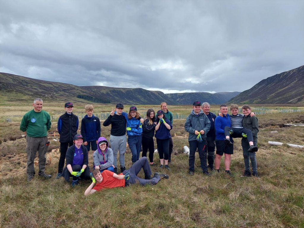Group of junior rangers smiling for the camera with the Cairngorms behind them on a cloudy day