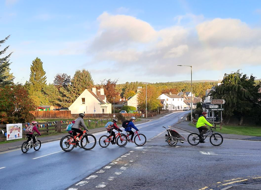 Adults and children cycling through Carrbridge as part of the Carrbridge Primary School 'bike bus'.