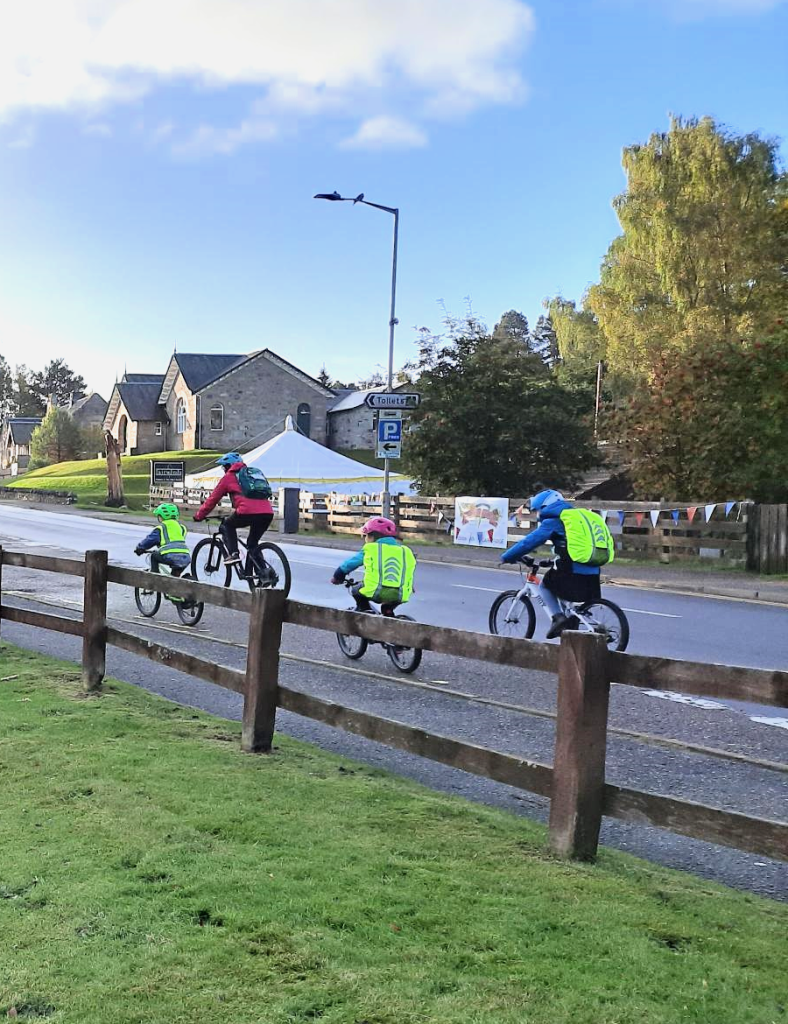 An adult and three children cycling through Carrbridge as part of the Carrbridge Primary School 'bike bus'.